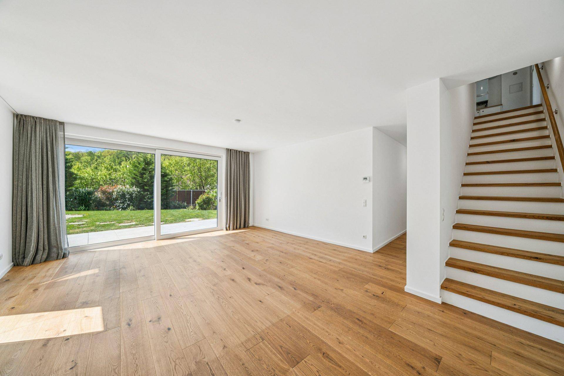 Geräumiges Wohnzimmer mit Holzboden, großen Fenstern und Treppe zum Obergeschoss.
