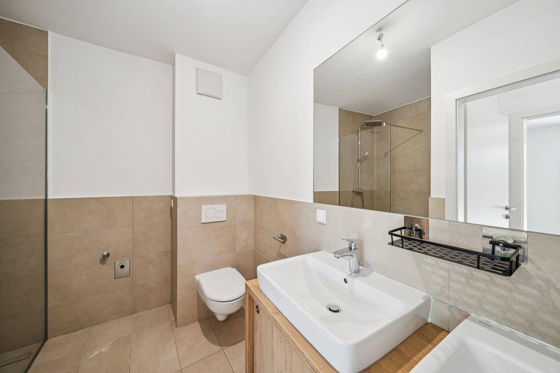 Modernes Badezimmer mit beigefarbenen Fliesen, ebenerdiger Dusche und wandhängendem WC.
