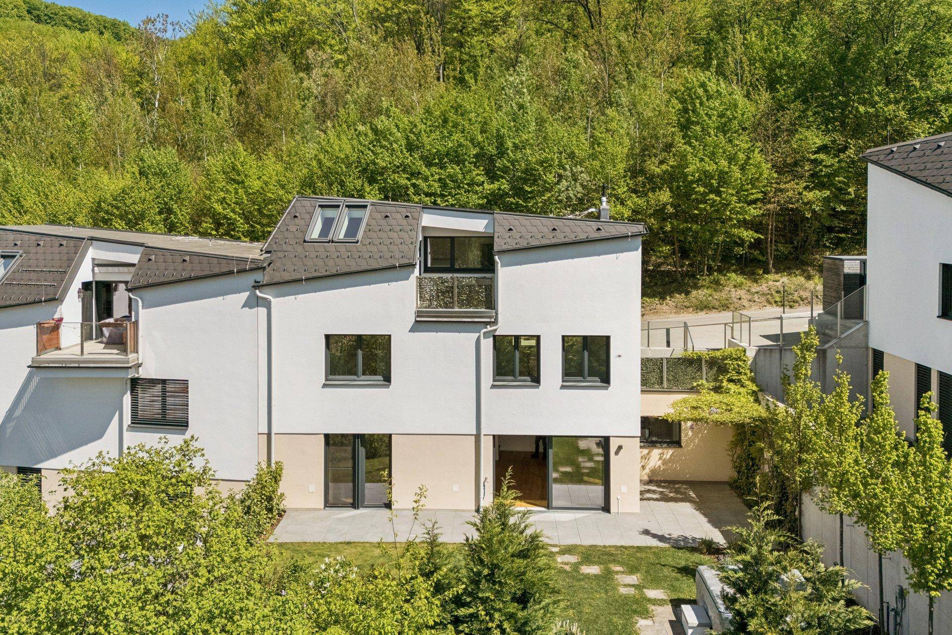 Ansicht eines modernen Reihenhauses mit Balkon, Dachfenstern und Gartenbereich.