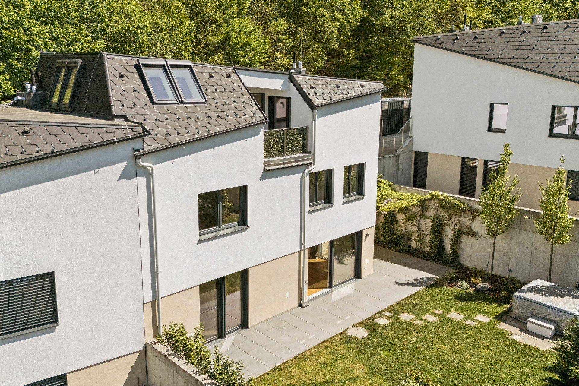 Vogelperspektive auf ein modernes Wohnhaus mit Terrasse, Garten und angrenzendem Wald.