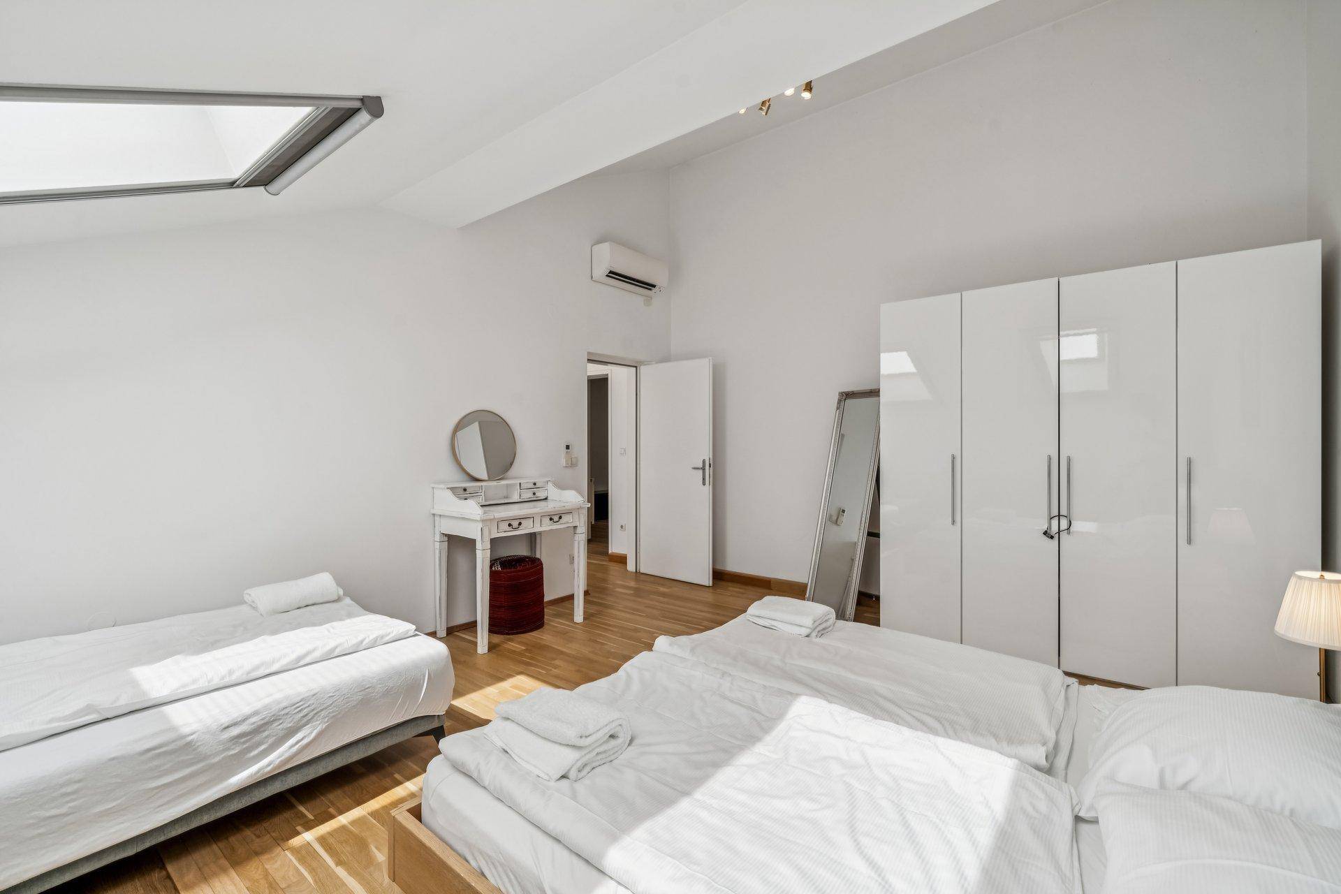 Helles Schlafzimmer im Dachgeschoss mit Holzfußboden, Dachfenster und weißem Kleiderschrank.