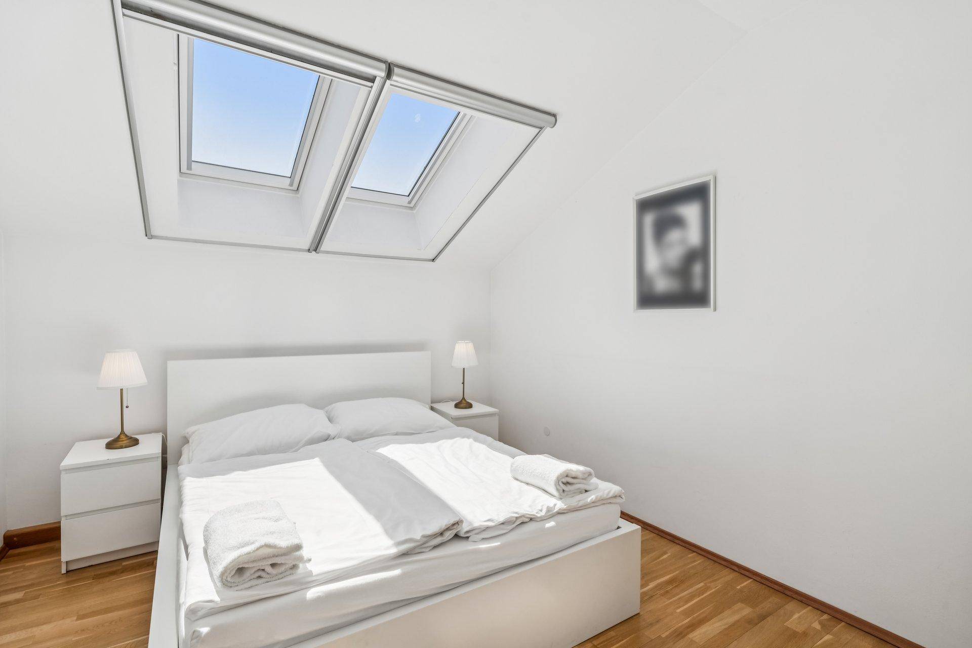 Gemütliches Schlafzimmer mit zwei Dachfenstern, Holzfußboden und minimalistischer Einrichtung.