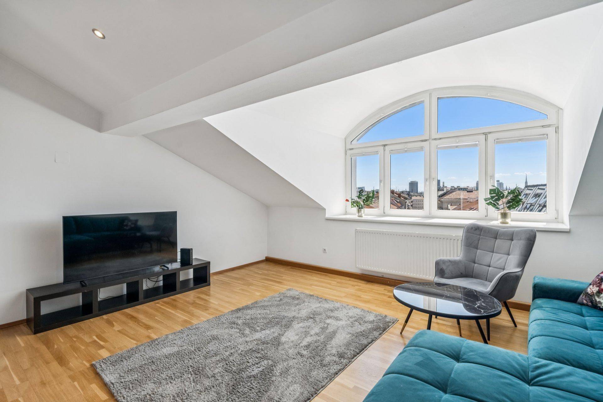 Geräumiges Wohnzimmer mit Holzfußboden, großem Fenster und Blick auf die Stadt.
