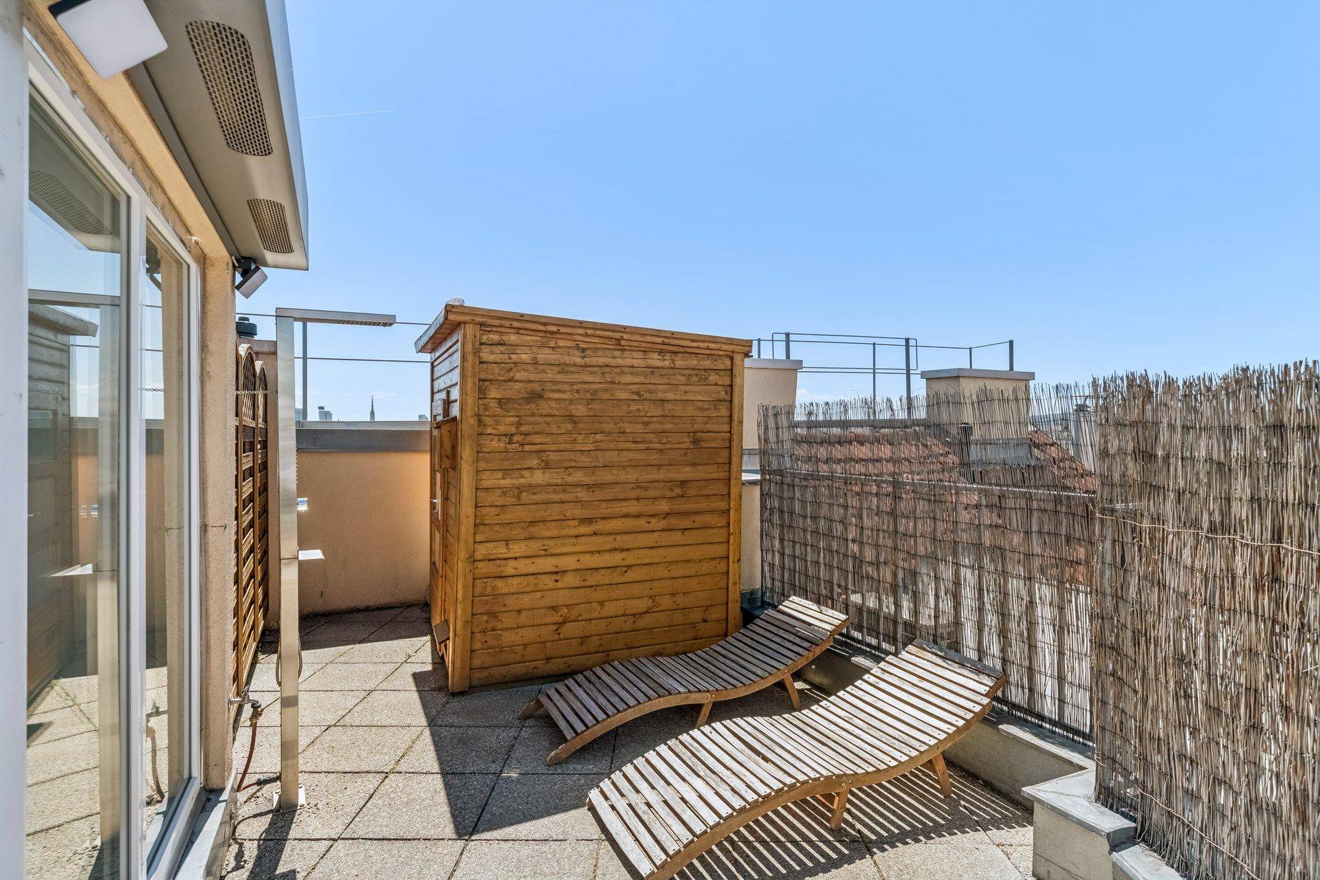 Sonniger Bereich der Dachterrasse mit Holzliegen und einer kleinen Saunakabine.