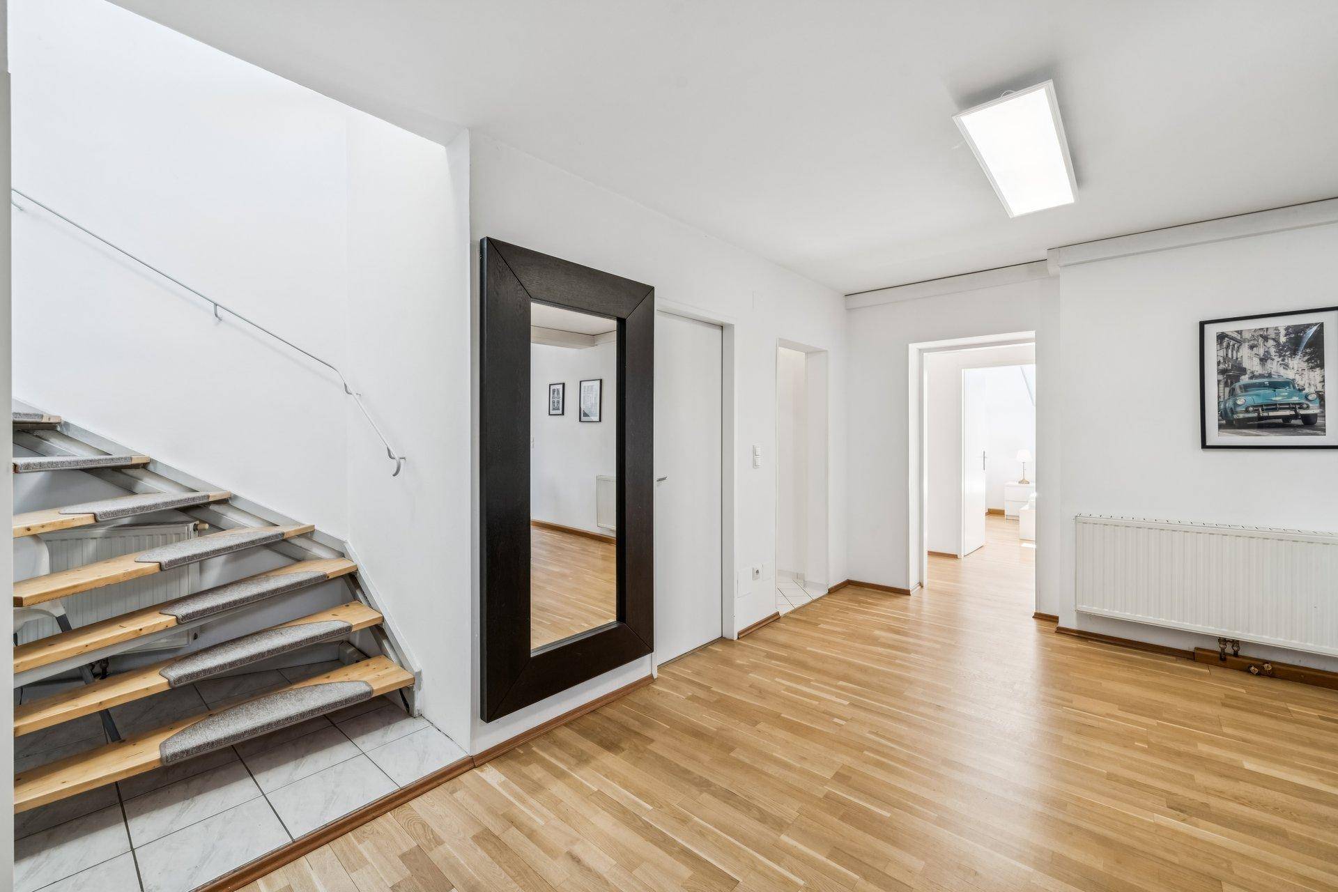 Geräumiger Flur mit Holzfußboden, Treppenaufgang und großem Wandspiegel.