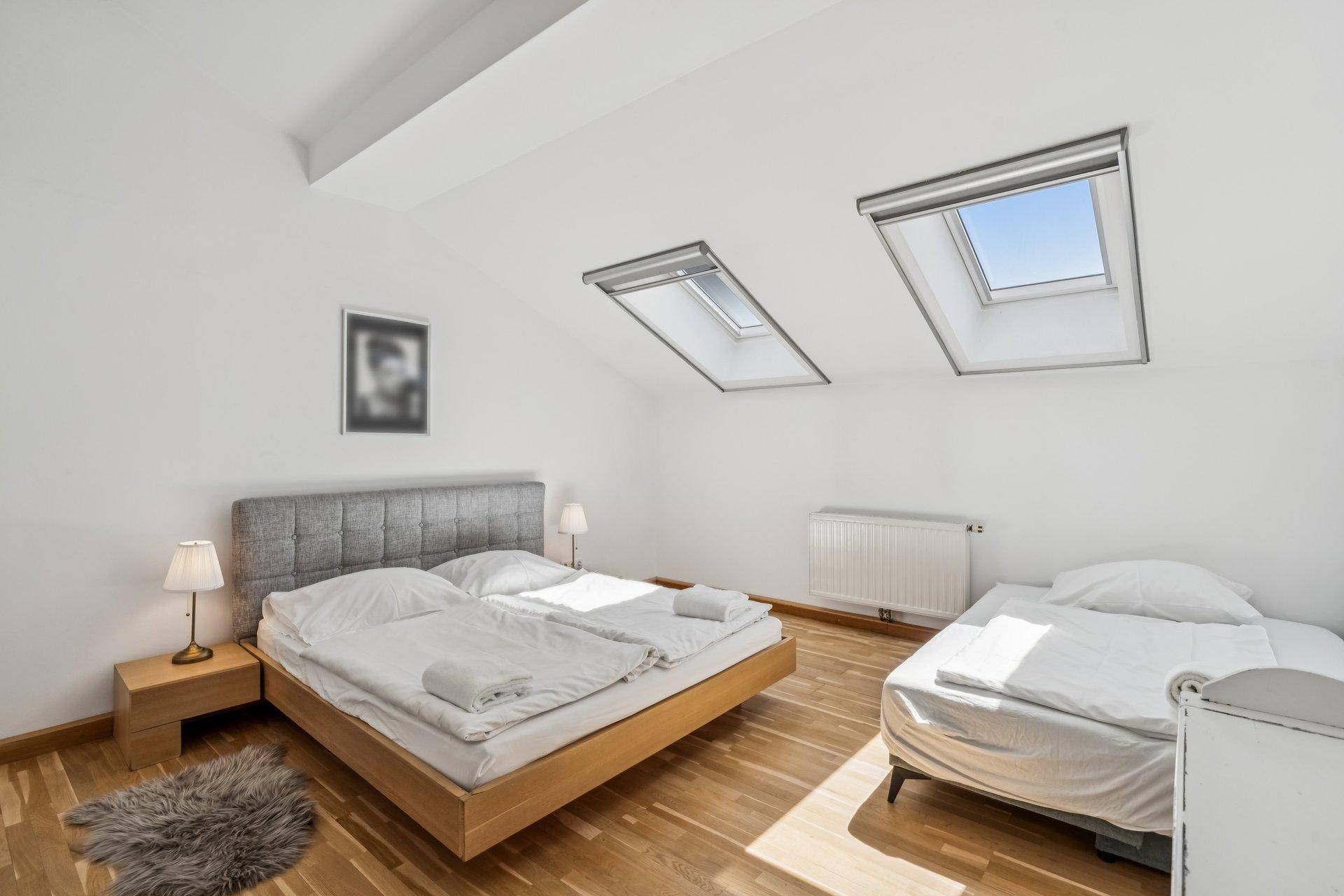 Helles Schlafzimmer mit Holzfußboden, zwei Dachfenstern und modernem Bett.