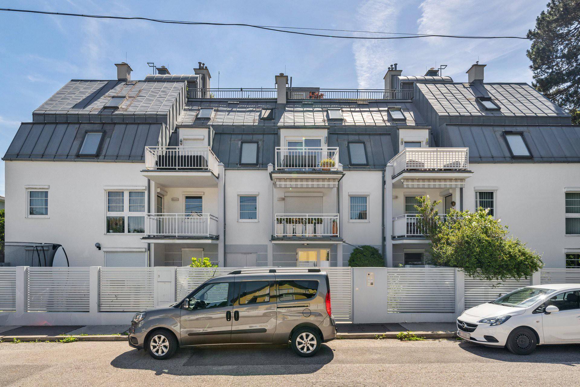 Mehrfamilienhaus mit moderner Architektur, Balkonen und Mansarddach.