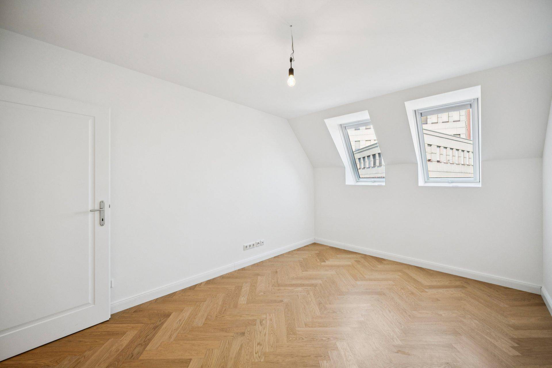 Leerer Raum mit Dachschrägen, Parkettboden und zwei Dachfenstern.