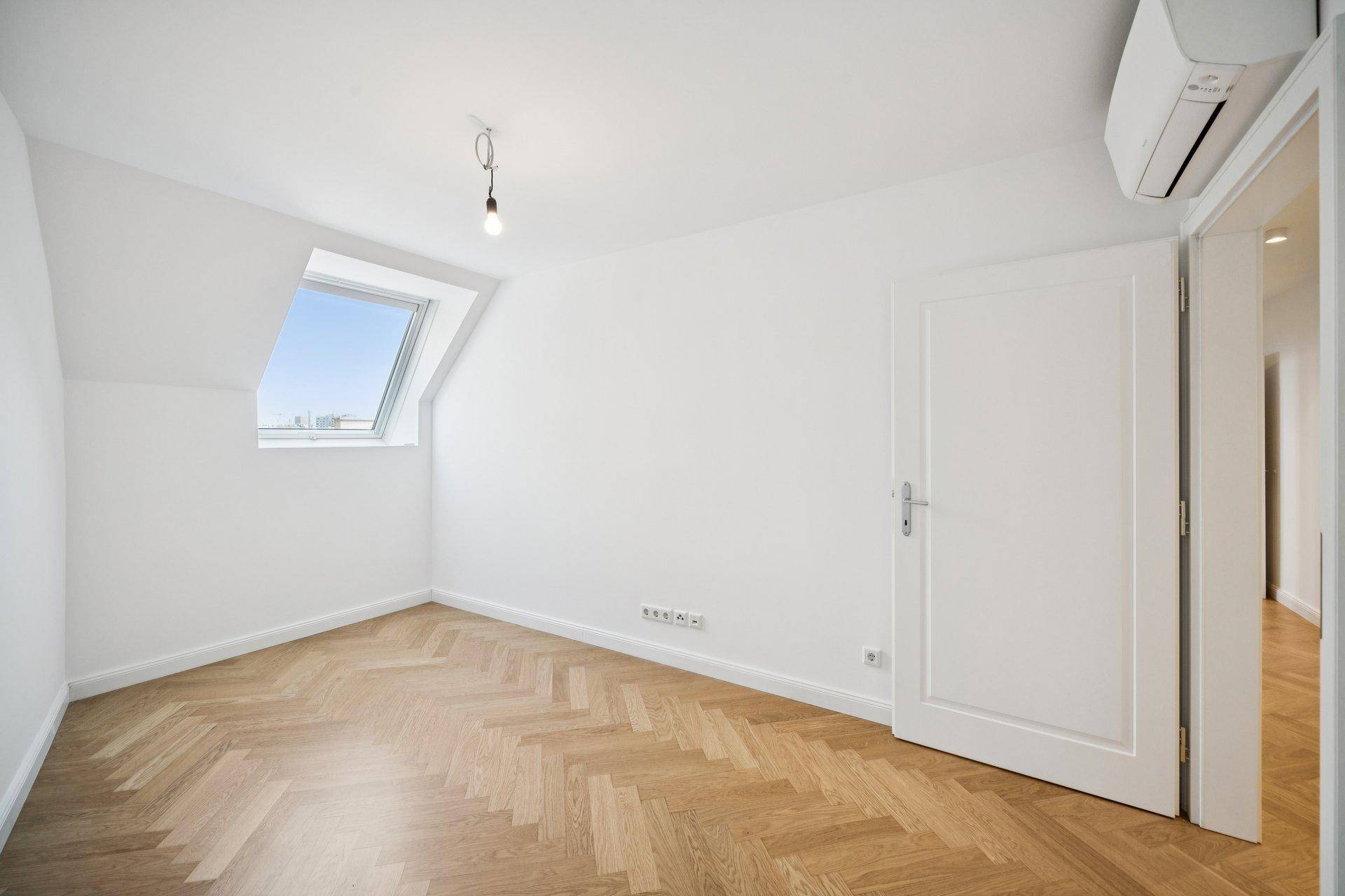 Leerer Raum mit Dachschräge, Parkettboden und einem Dachfenster.