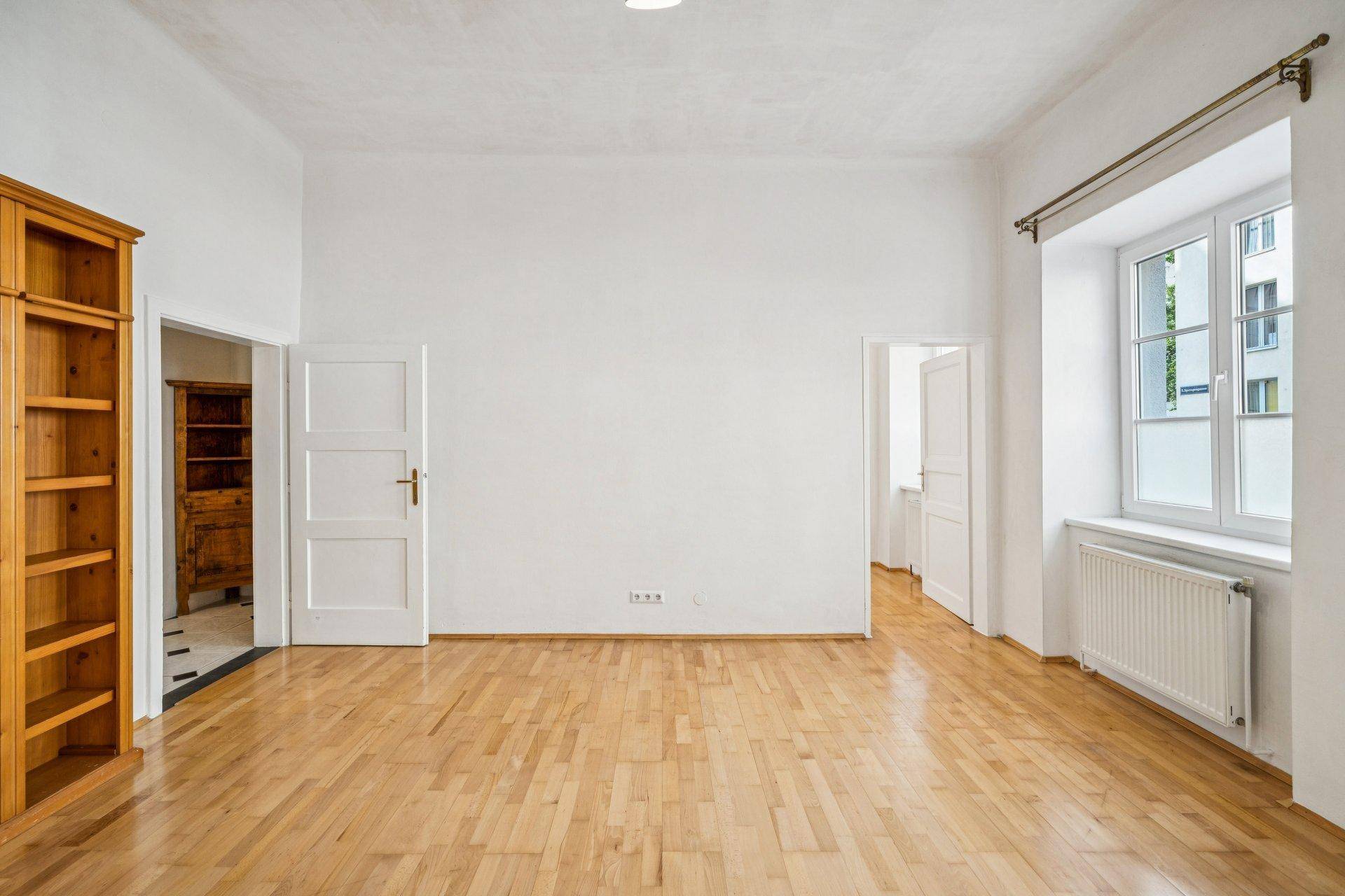 Heller Raum mit Parkettboden, hohen Decken und Zugang zu weiteren Zimmern.