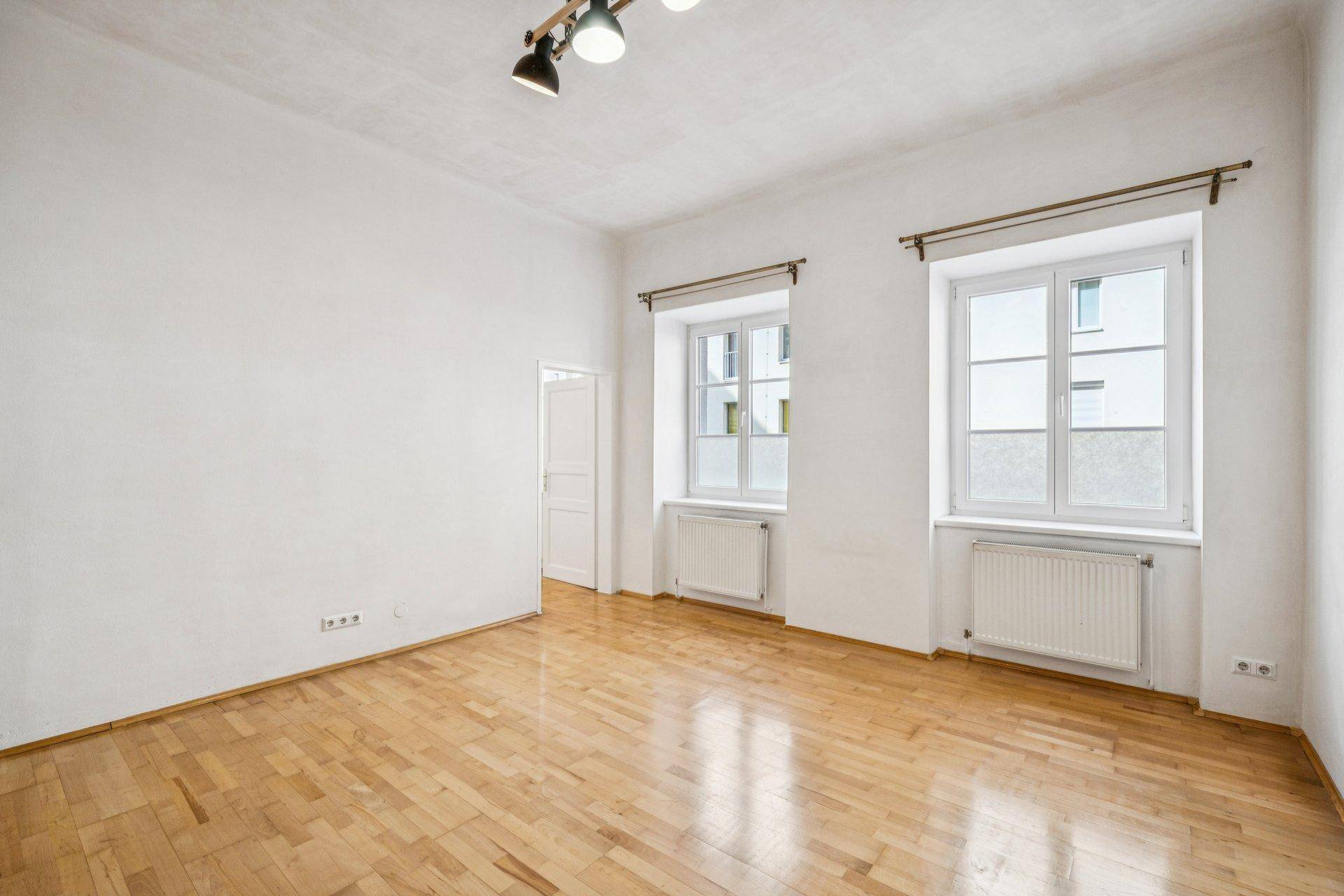 Lichtdurchflutetes Zimmer mit Parkettboden und zwei Fenstern, bietet vielseitige Nutzungsmöglichkeiten.