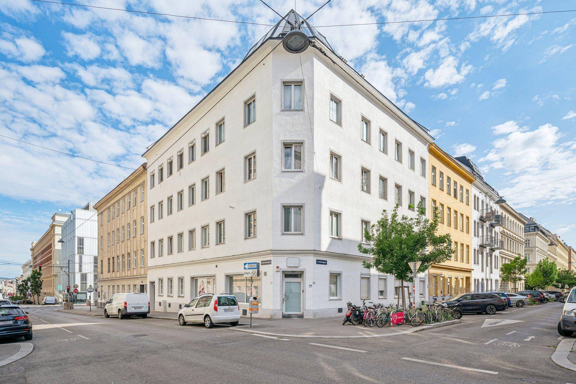 Eckgebäude in urbaner Umgebung mit klassischer Architektur und vielen Fenstern.