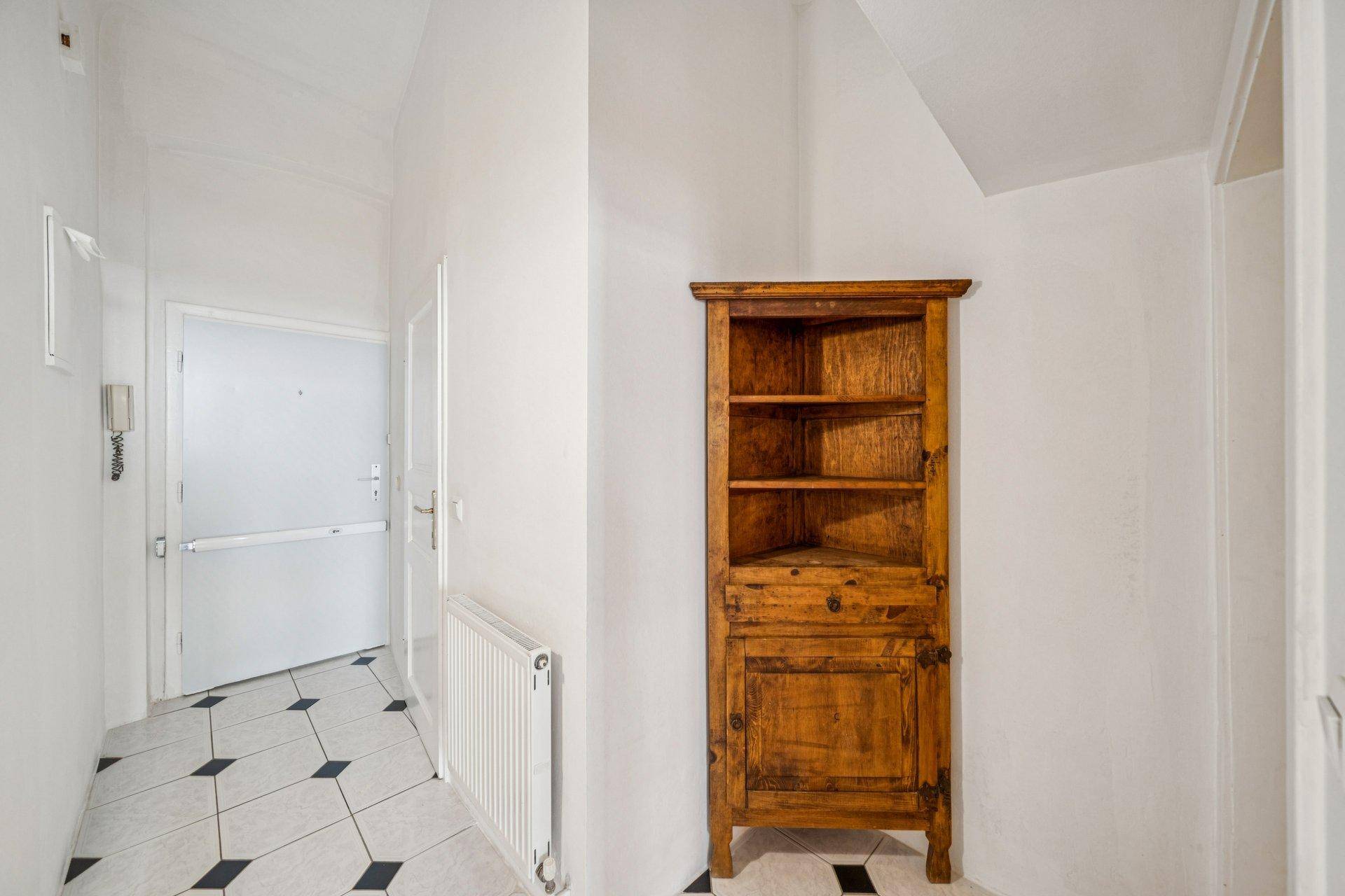 Flur mit Fliesenboden und einem rustikalen Eckschrank, führt zum Eingang.