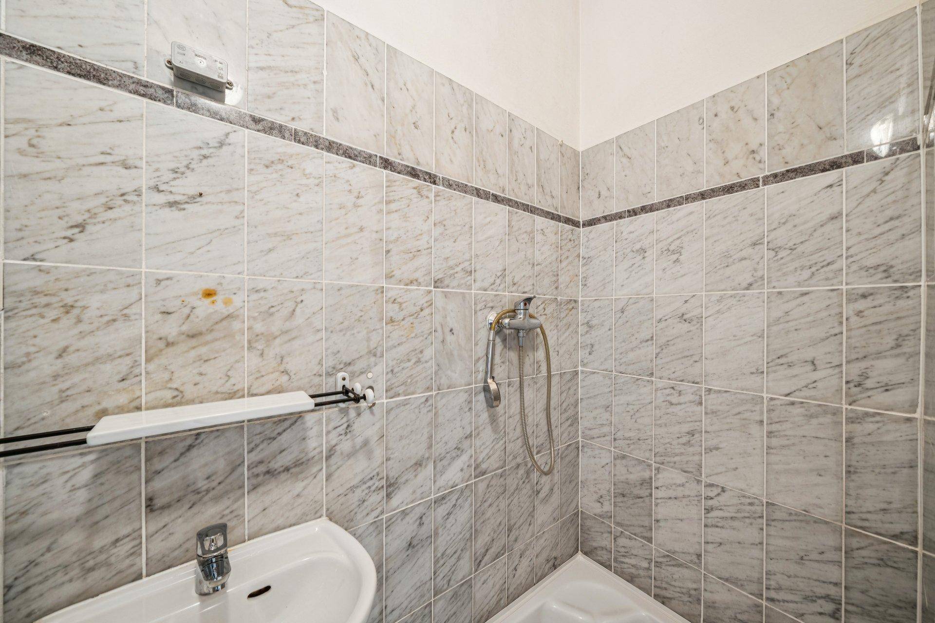 Badezimmer mit hellen Marmorfliesen und Duschbereich, funktional und gepflegt.