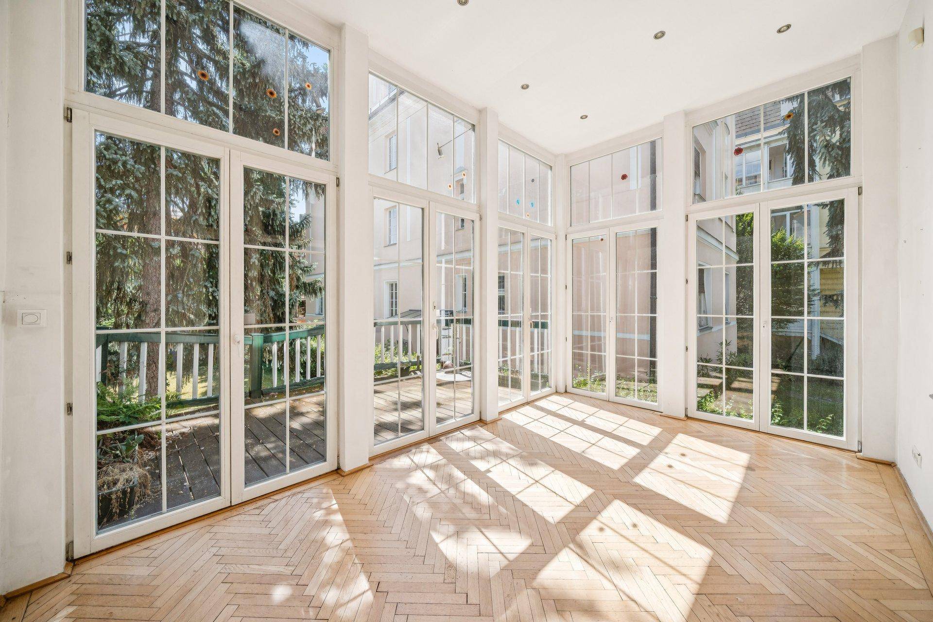 Lichtdurchfluteter Raum mit großen Glasfronten und Zugang zu einem Balkon.