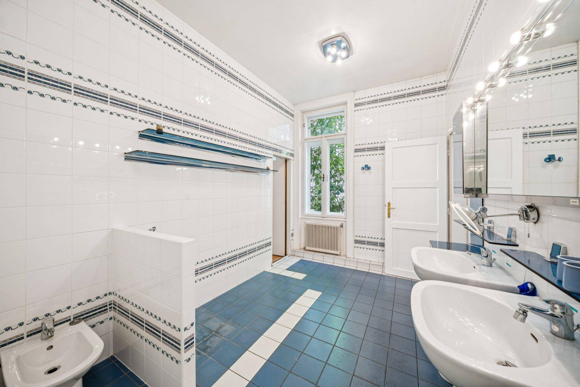 Geräumiges Badezimmer mit Doppelwaschbecken, Bidet und blauen Fliesen im 80er-Jahre-Stil.