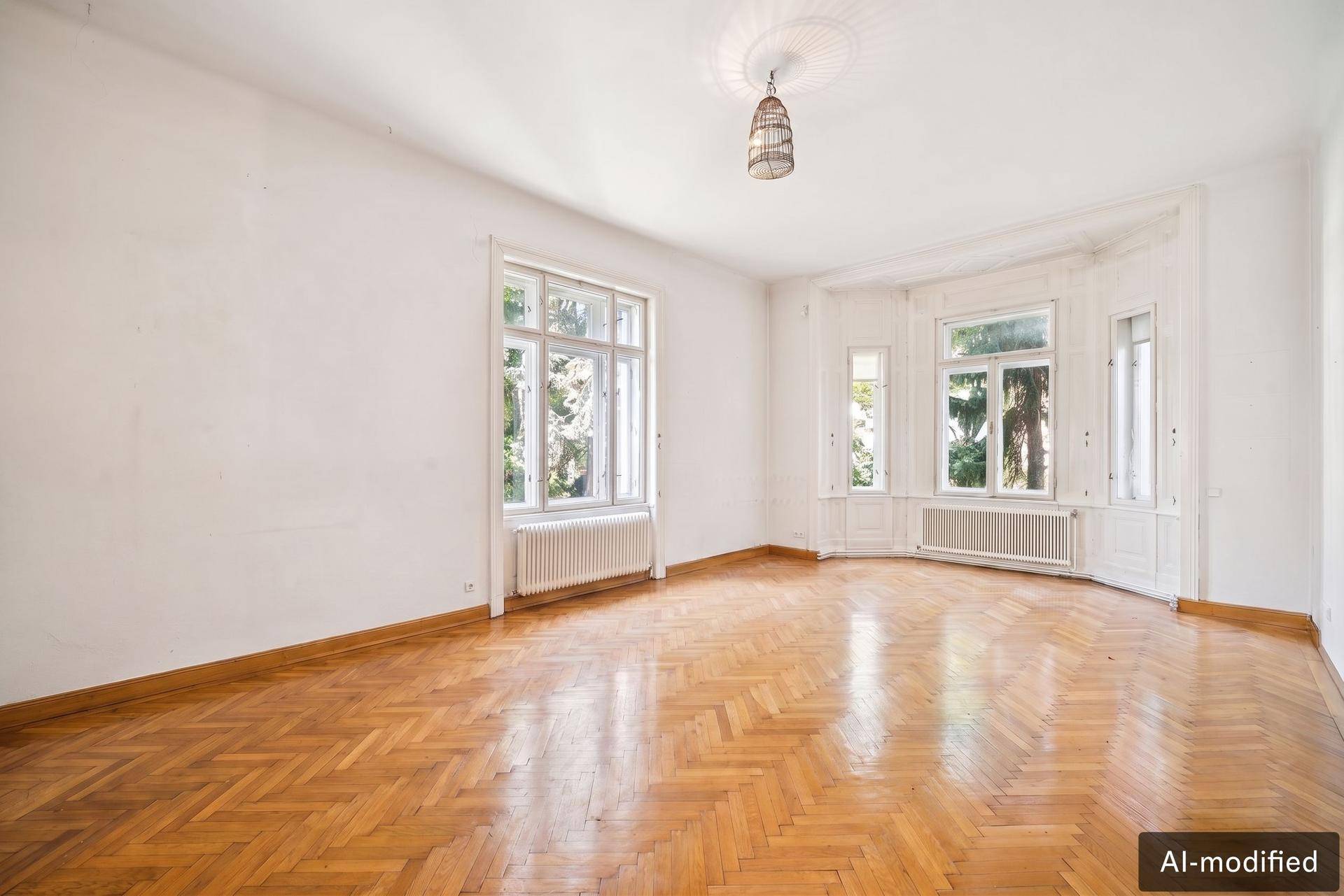 Geräumiges Wohnzimmer mit Fischgrätparkett, Erkerfenstern und Stuckdecke.