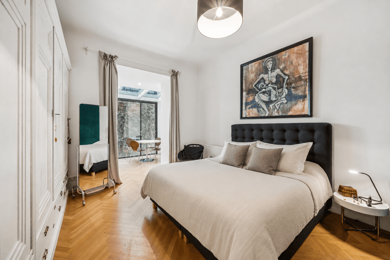 Gemütliches Schlafzimmer mit Doppelbett, weißem Kleiderschrank und Zugang zu einem hellen Essbereich.