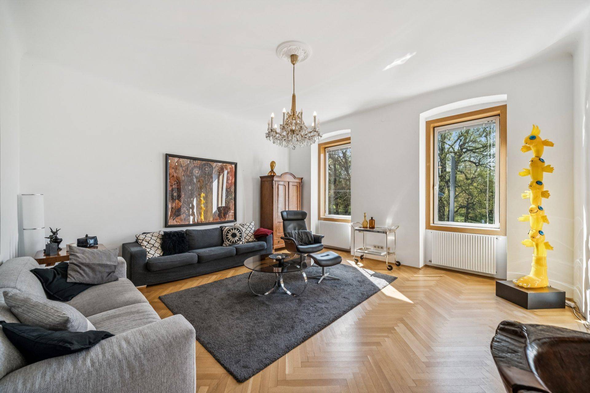 Helles Wohnzimmer mit bequemen Sofas, Fischgrätparkett und einem eleganten Kronleuchter.
