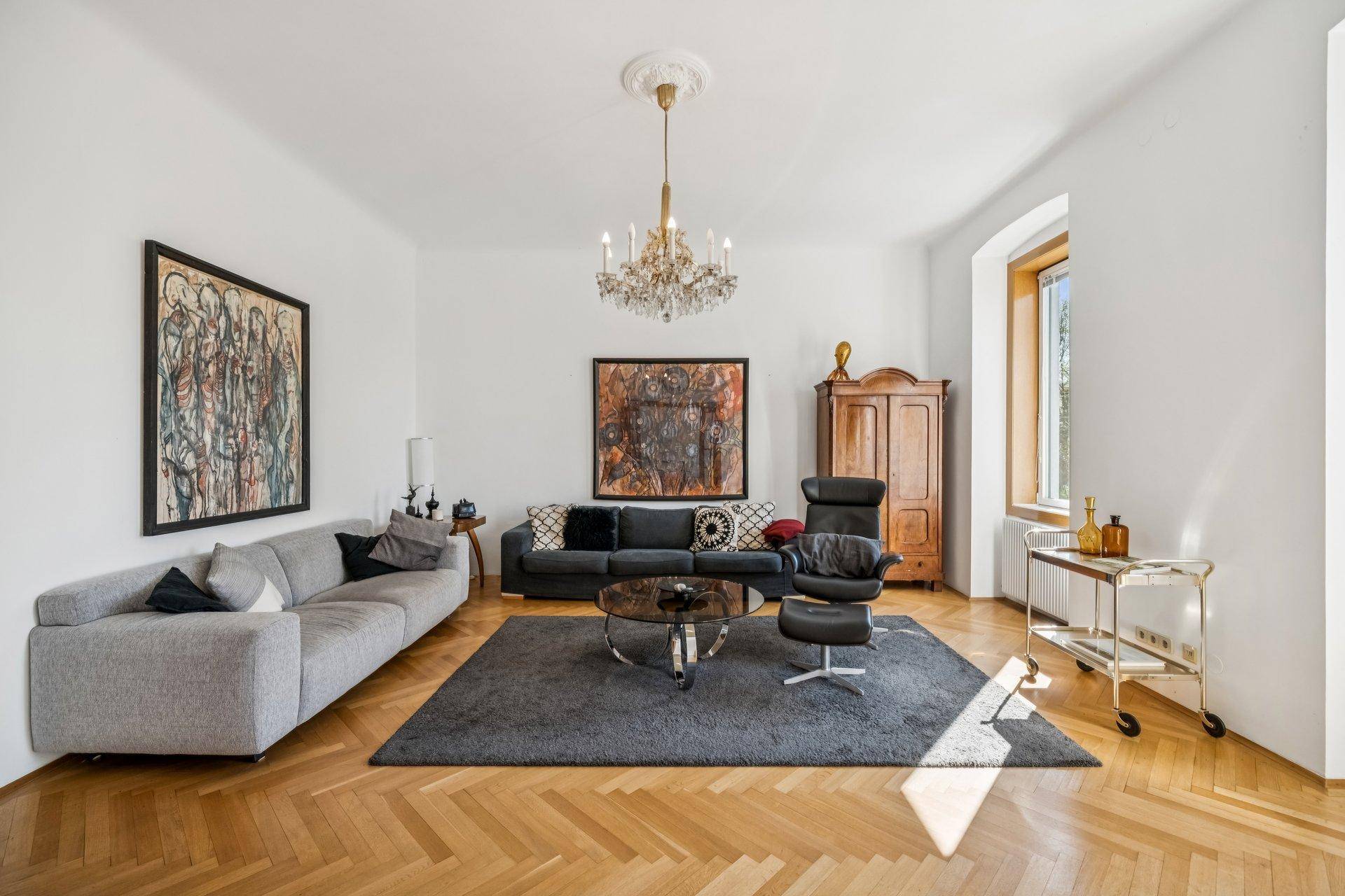 Geräumiges Wohnzimmer mit zwei Sofas, Fischgrätparkett und einem eleganten Kronleuchter.