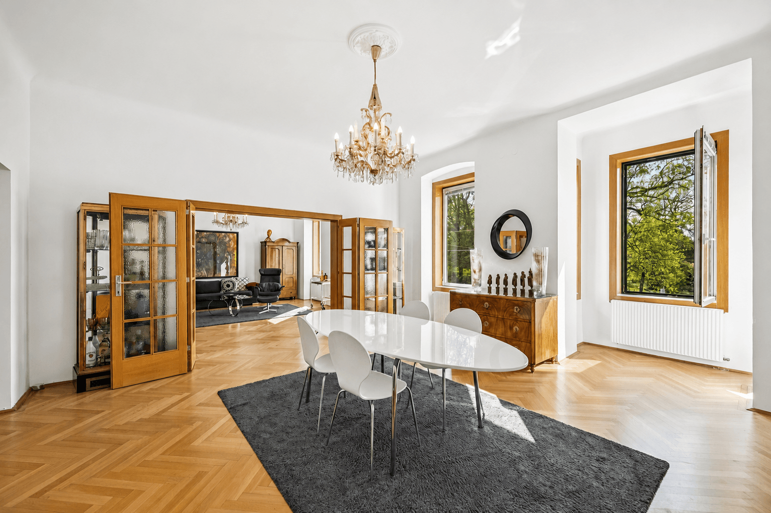 Elegantes Esszimmer mit Fischgrätparkett, Kronleuchter und Zugang zu einem weiteren Wohnbereich.