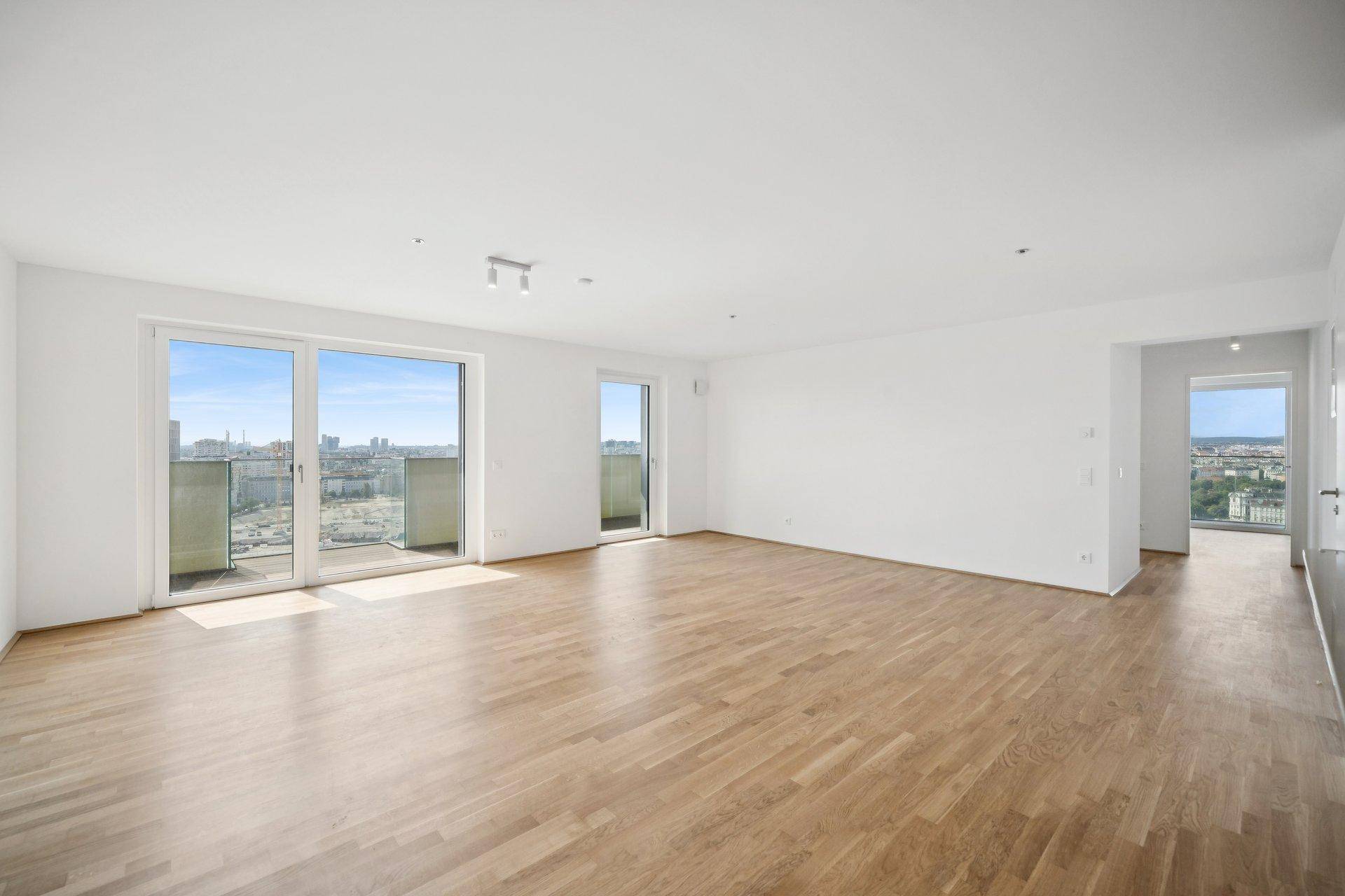 Heller, leerer Wohnraum mit Holzboden und großen Fenstern mit Stadtblick.