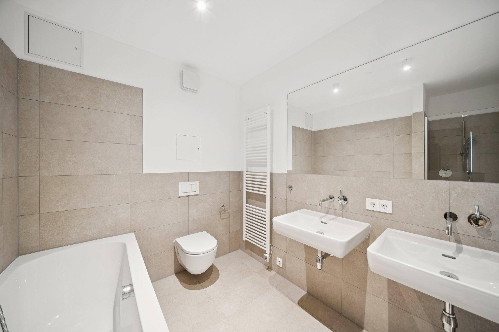 Modernes Badezimmer mit zwei Waschbecken, Badewanne, WC und beigefarbenen Fliesen.