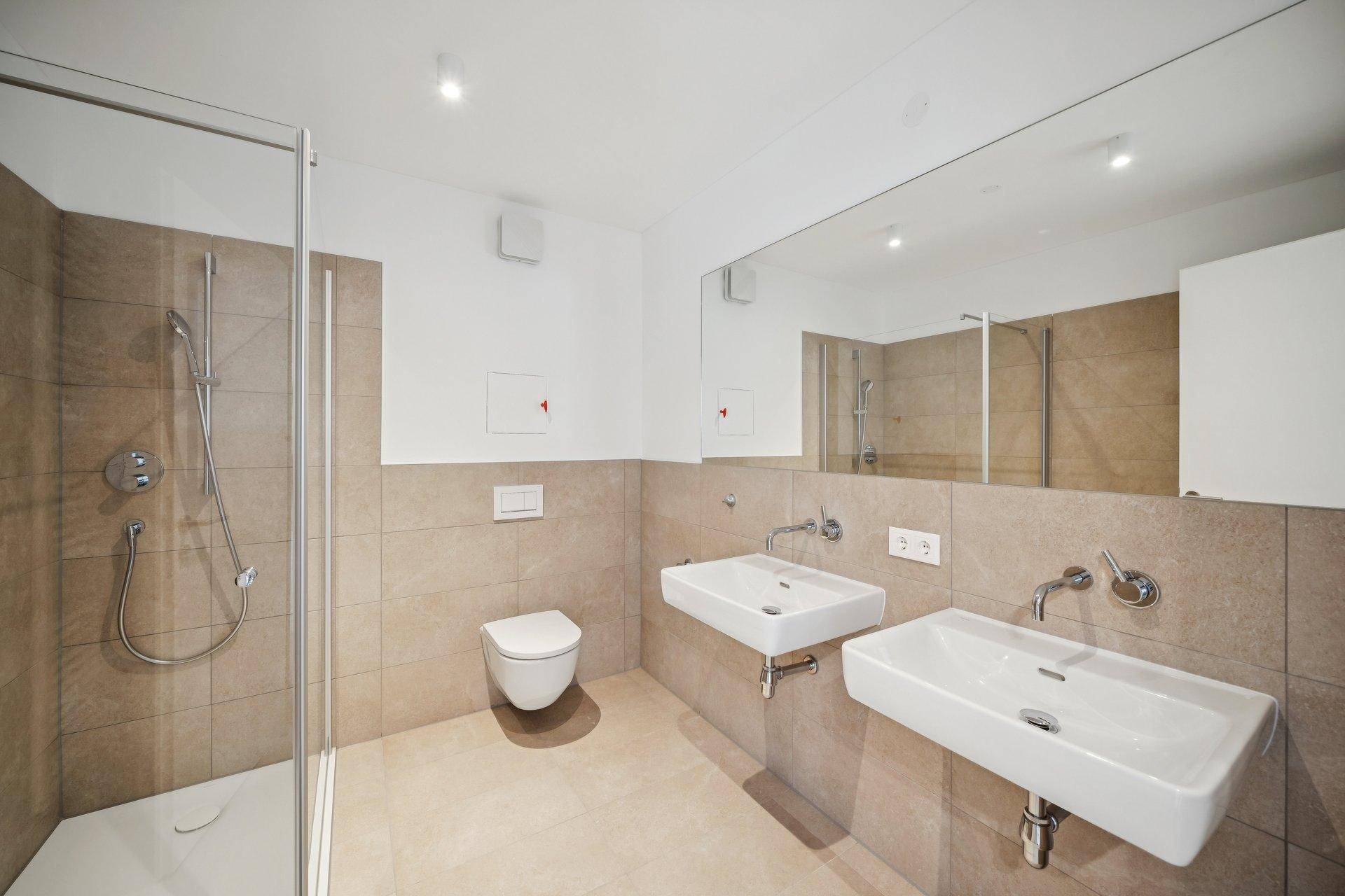 Modernes Badezimmer mit beigefarbenen Fliesen, ebenerdiger Dusche, Wand-WC und Doppelwaschbecken.