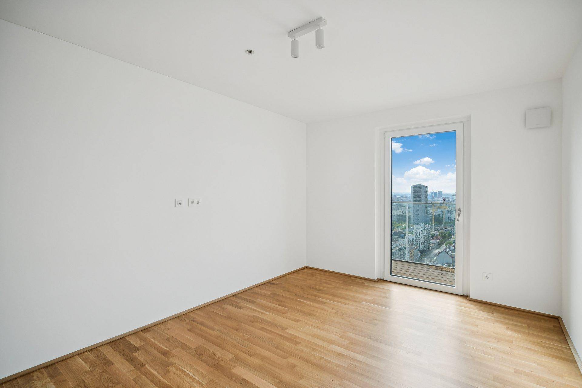 Helles Zimmer mit Eichenparkett und großem Fenster, das einen weiten Blick über die Stadt bietet.
