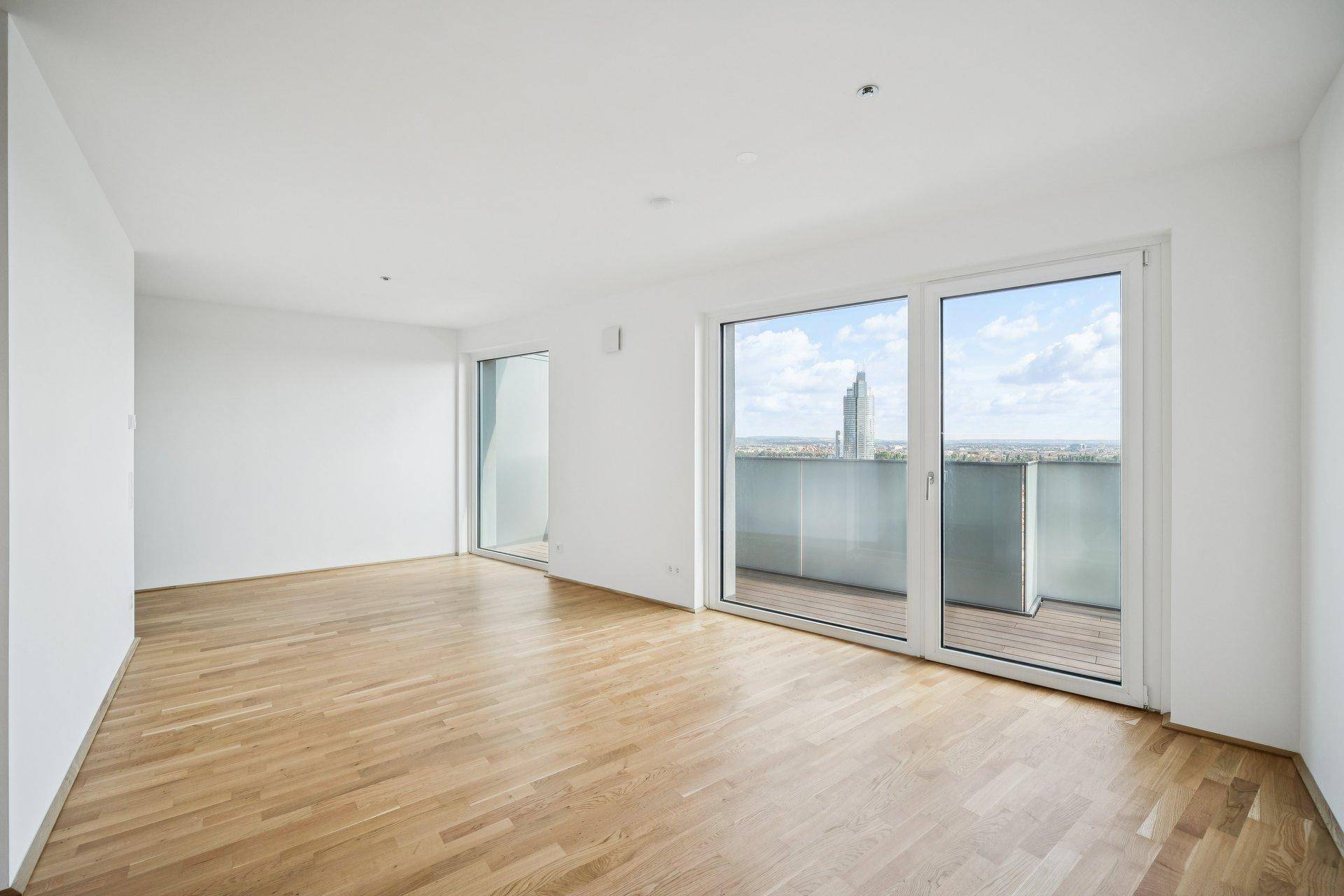 Heller, unmöblierter Wohnbereich mit Parkettboden und großen Schiebetüren zum Balkon.