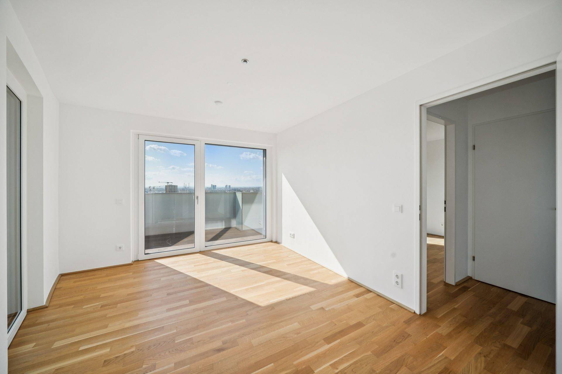 Helles, unmöbliertes Schlafzimmer mit Parkettboden und Zugang zum Balkon.
