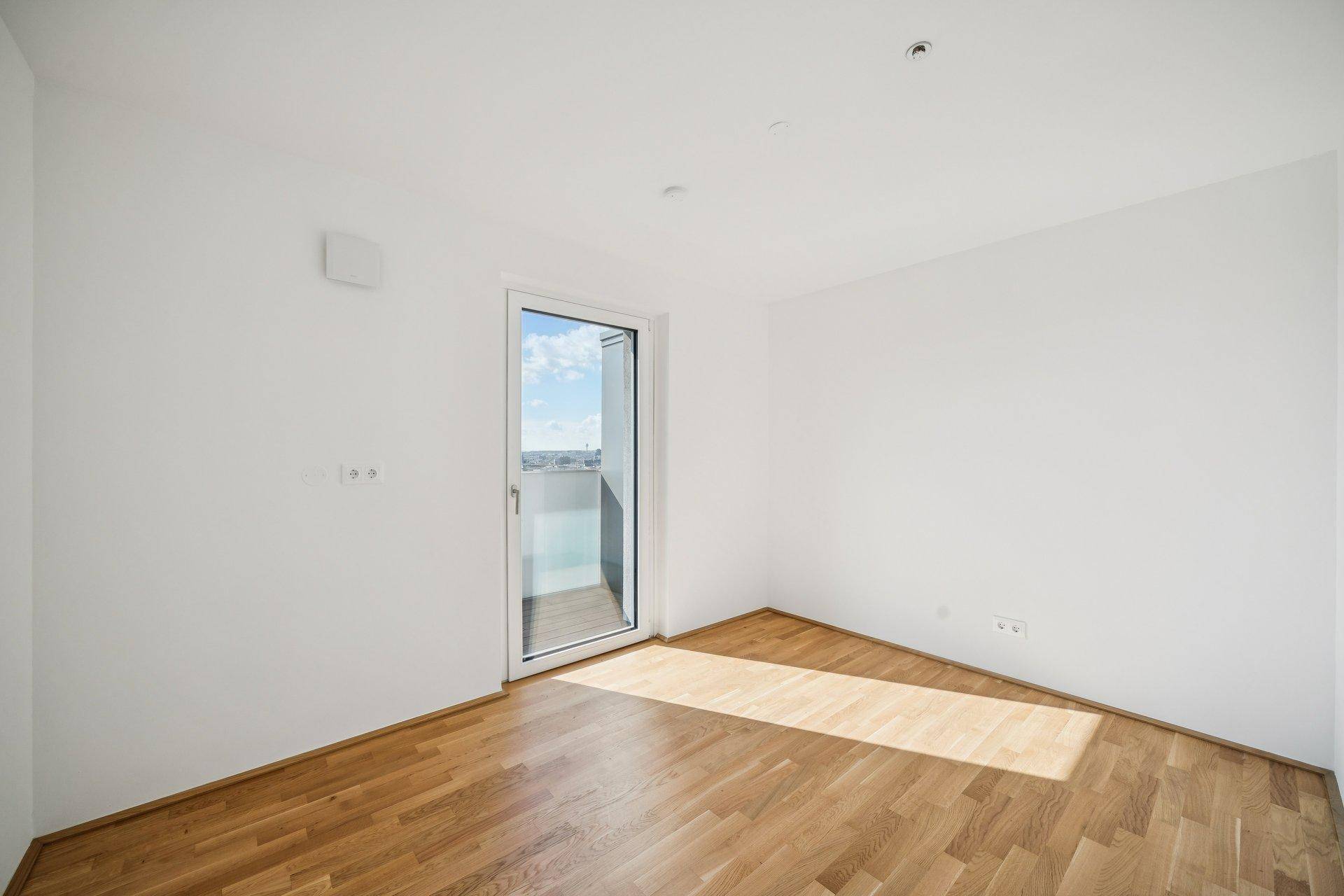 Unmöbliertes Schlafzimmer mit Parkettboden und Zugang zu einem kleinen Balkon.