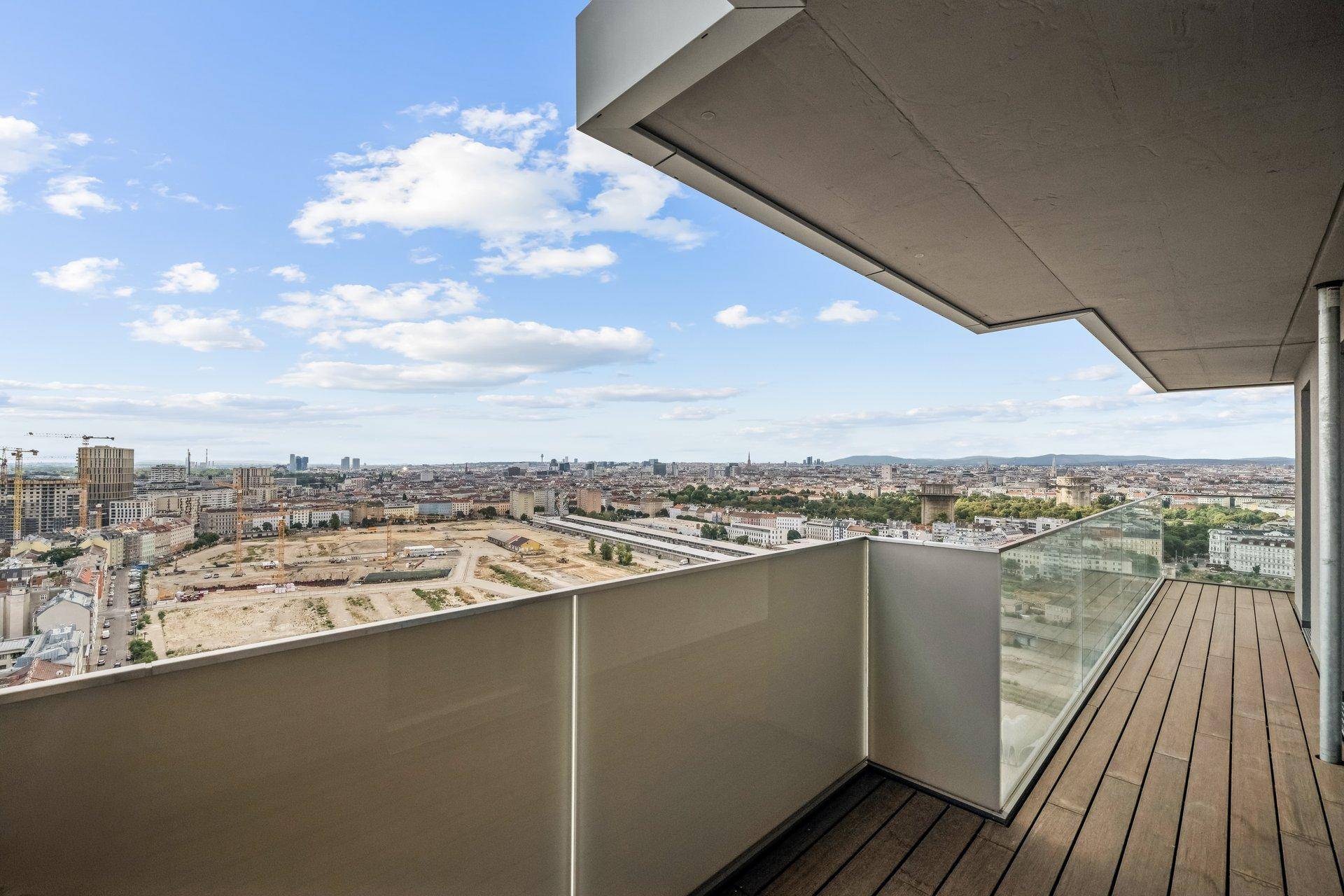 Geräumiger Balkon mit Holzdeck und Glasgeländer bietet einen weiten Blick über die Stadt.