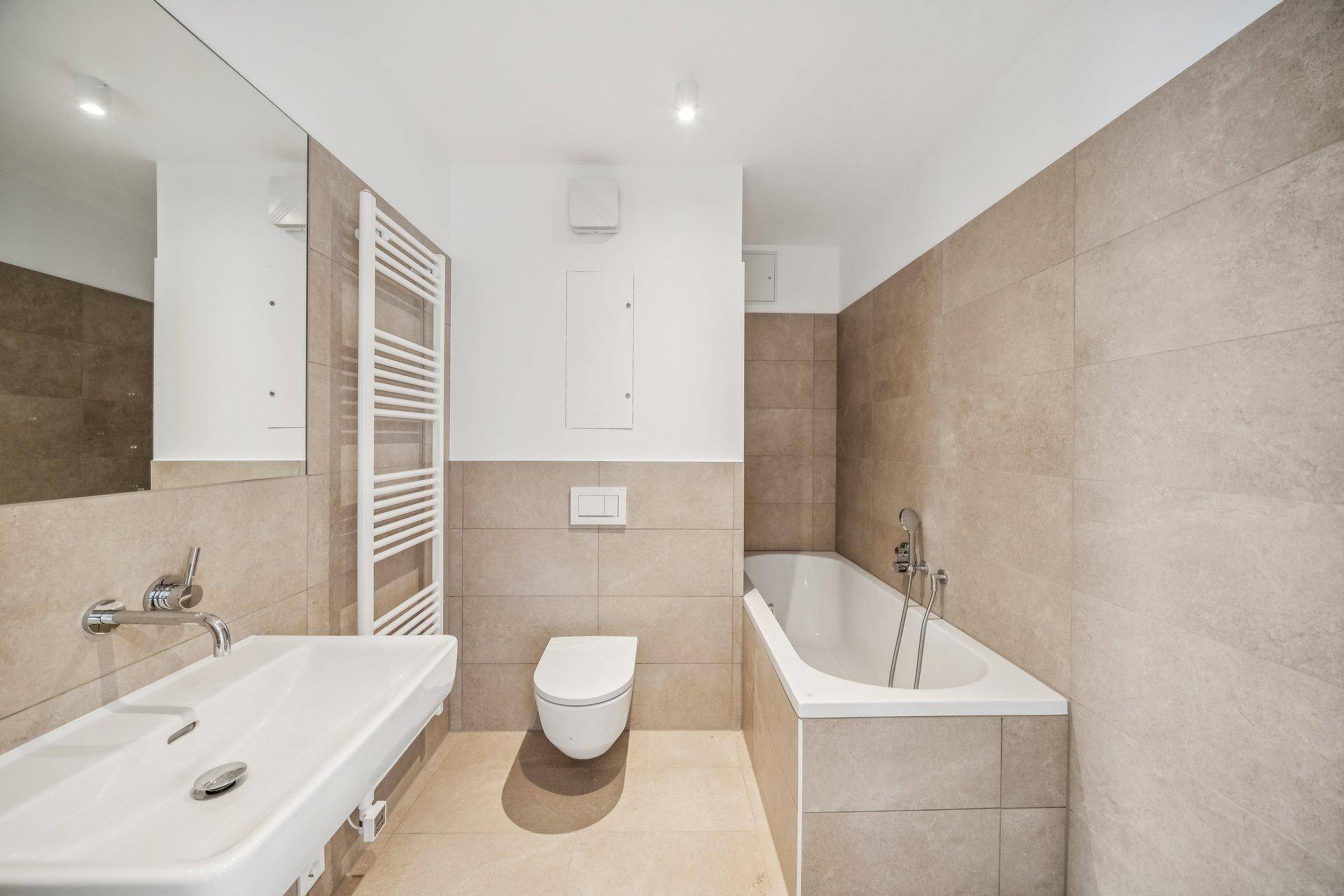 Modernes Badezimmer mit Badewanne, Einzelwaschbecken und beheiztem Handtuchhalter.