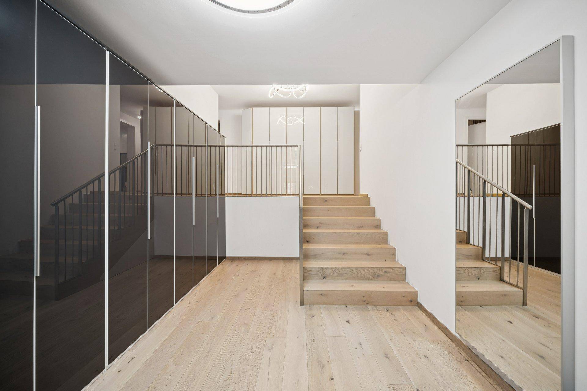 Heller Flur mit Holztreppe, integrierten Schränken und einem großen Spiegel, der den Raum erweitert.