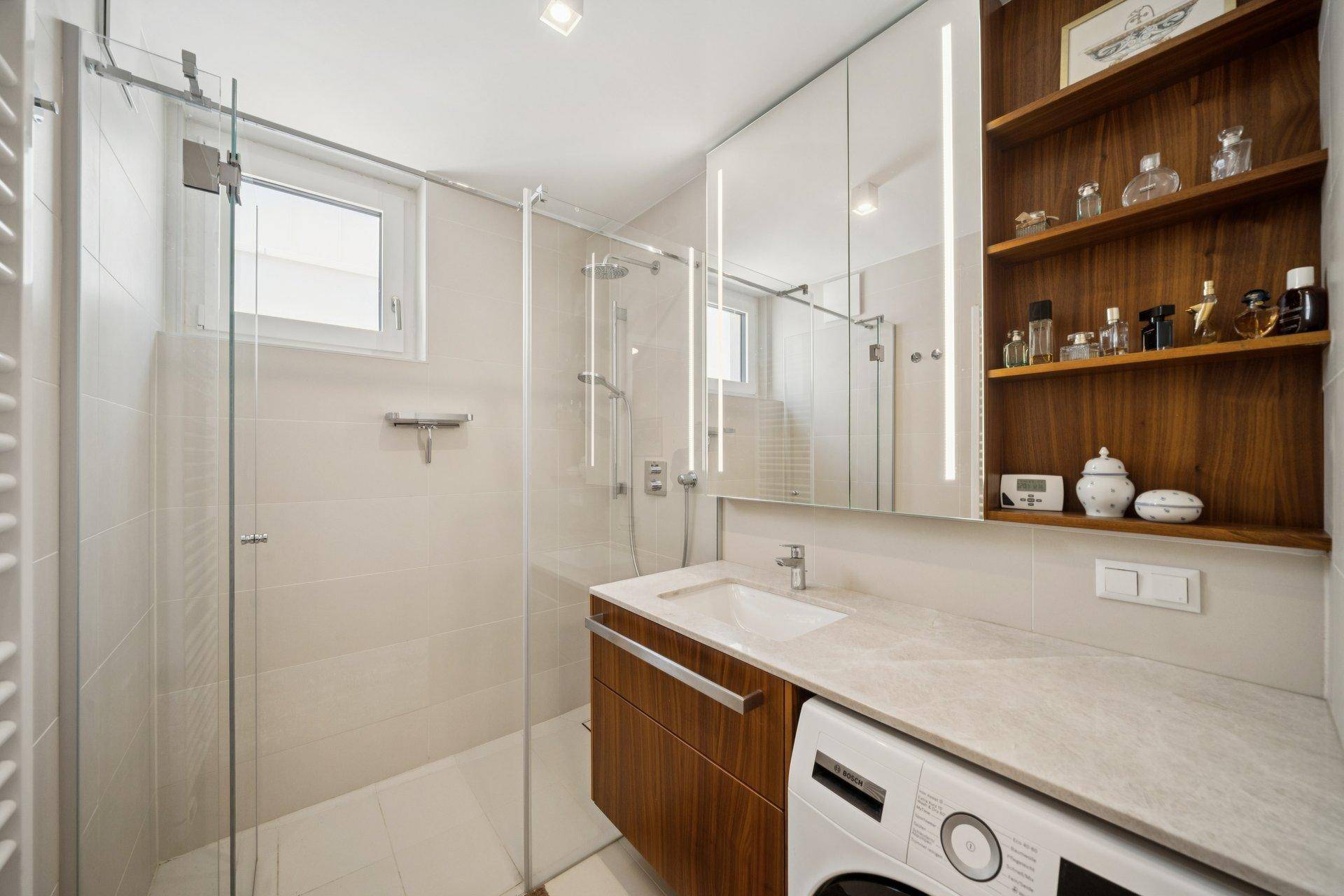 Modernes Badezimmer mit begehbarer Dusche, Waschbecken und integrierter Waschmaschine.