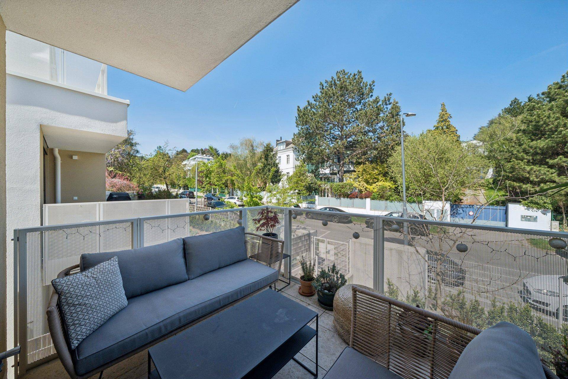 Möblierter Balkon mit Sitzgelegenheiten und Blick auf die grüne Umgebung und die Straße.