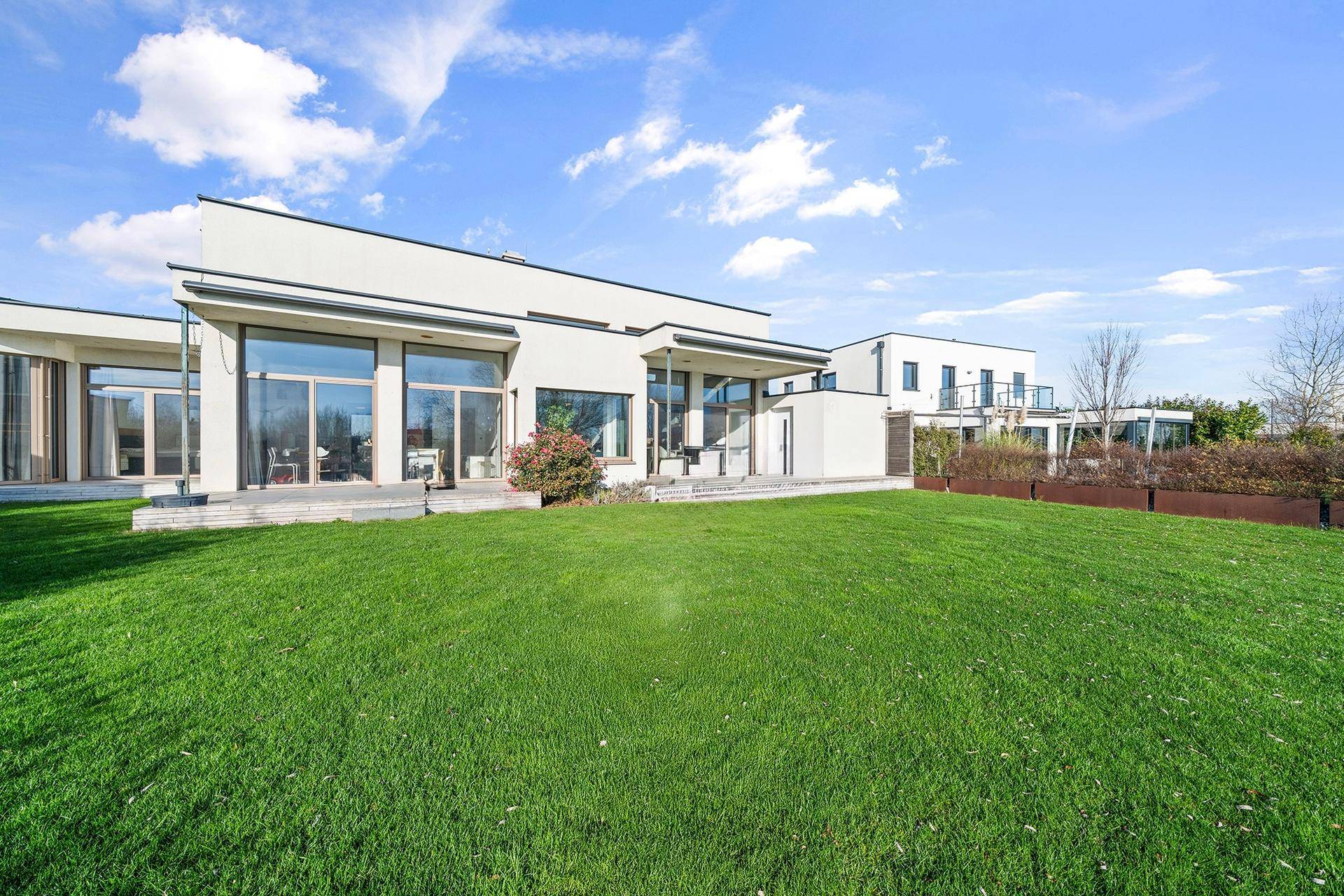 Moderne Architektur des Hauses mit weitläufigem Rasenbereich und großen Fensterfronten.