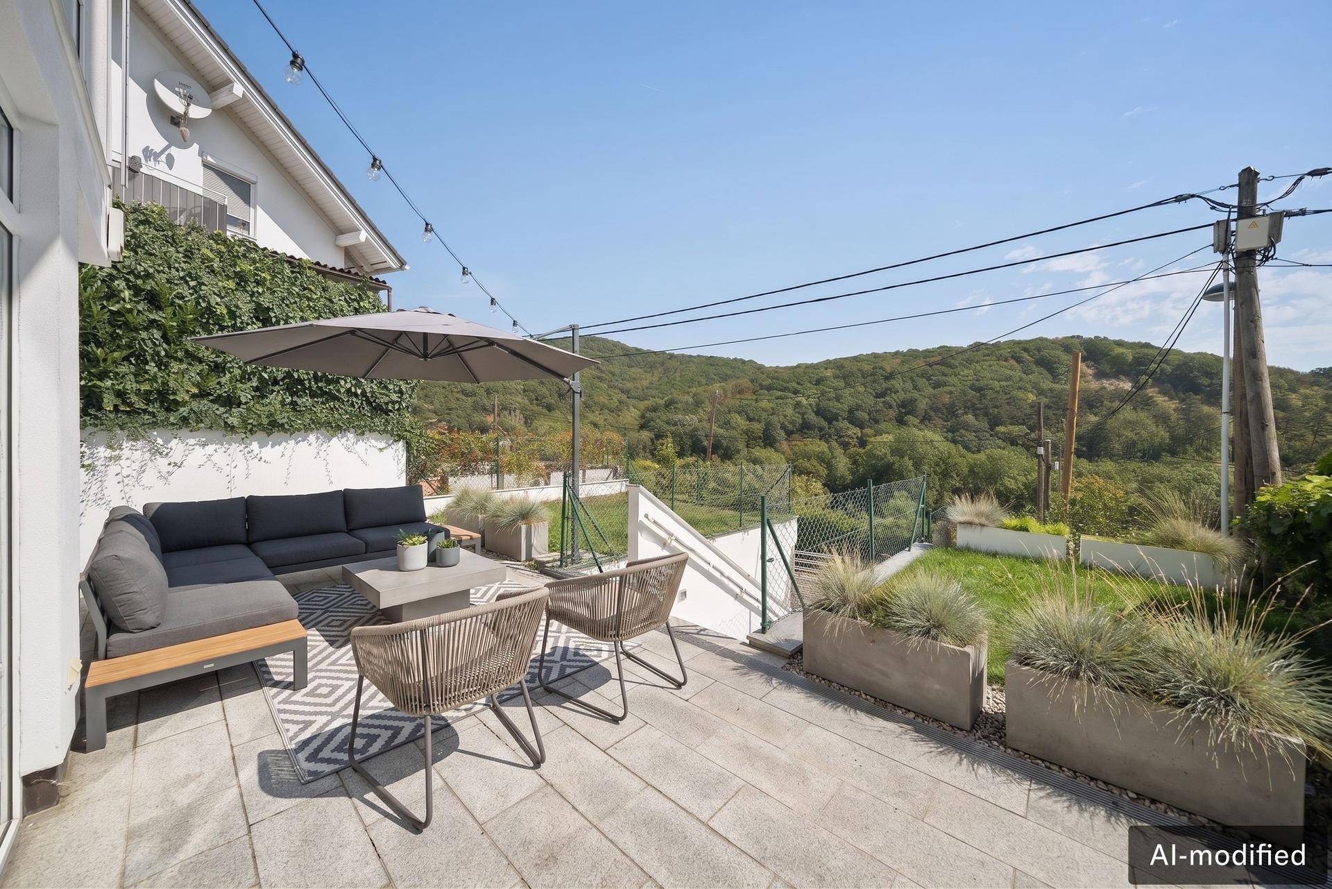 Gemütliche Terrasse mit Lounge-Sofa und Sonnenschirm, umgeben von viel Grün und Hügellandschaft.