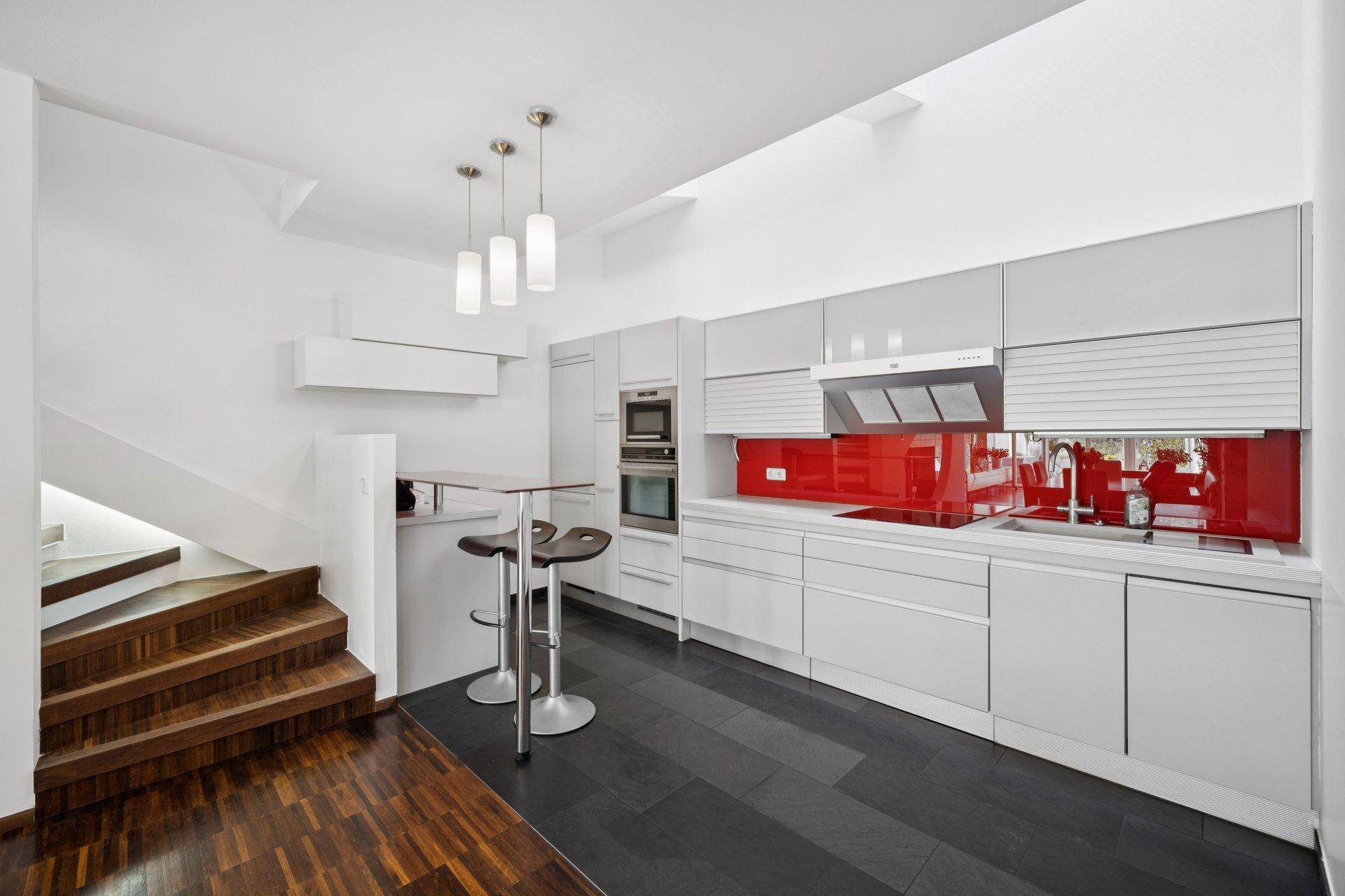 Moderne weiße Küche mit roter Rückwand und integrierten Geräten, inklusive Frühstücksbar.