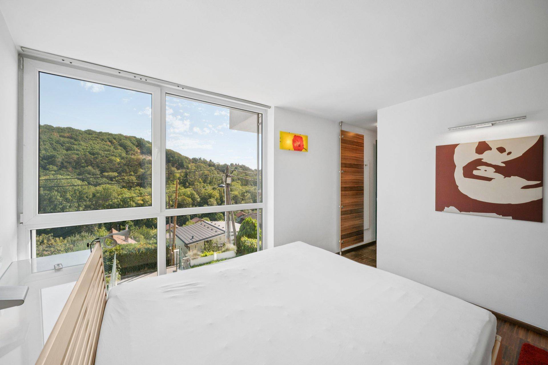 Schlafzimmer mit großen Fenstern und weitem Blick auf die bewaldete Umgebung.