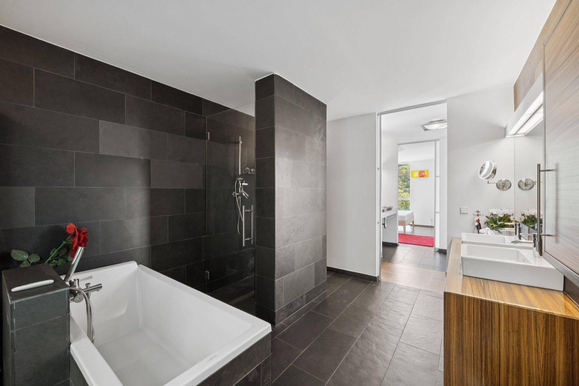 Geräumiges Badezimmer mit dunklen Fliesen, Badewanne und separater Dusche.
