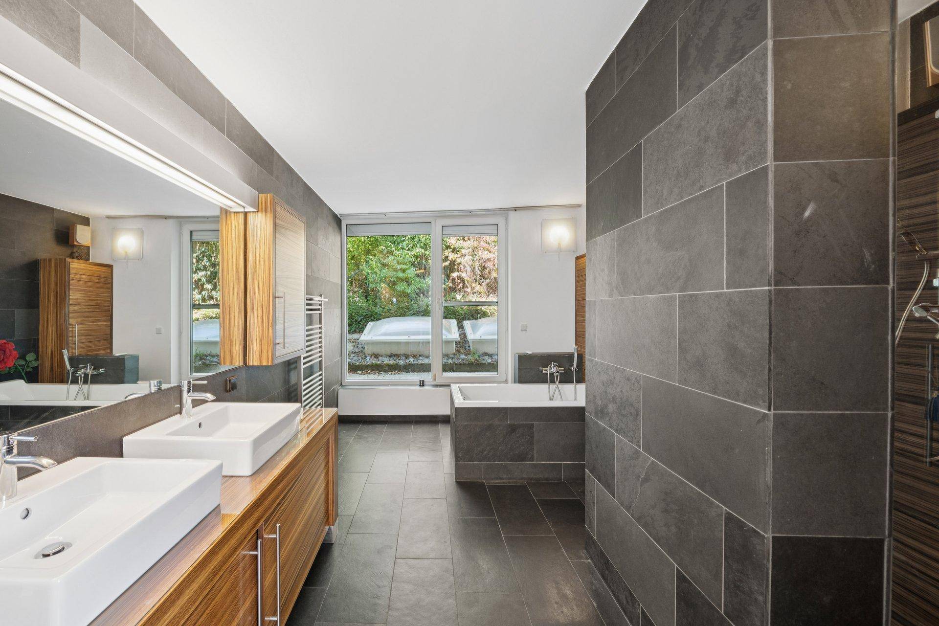 Modernes Badezimmer mit dunklen Fliesen, Doppelwaschbecken und Badewanne.