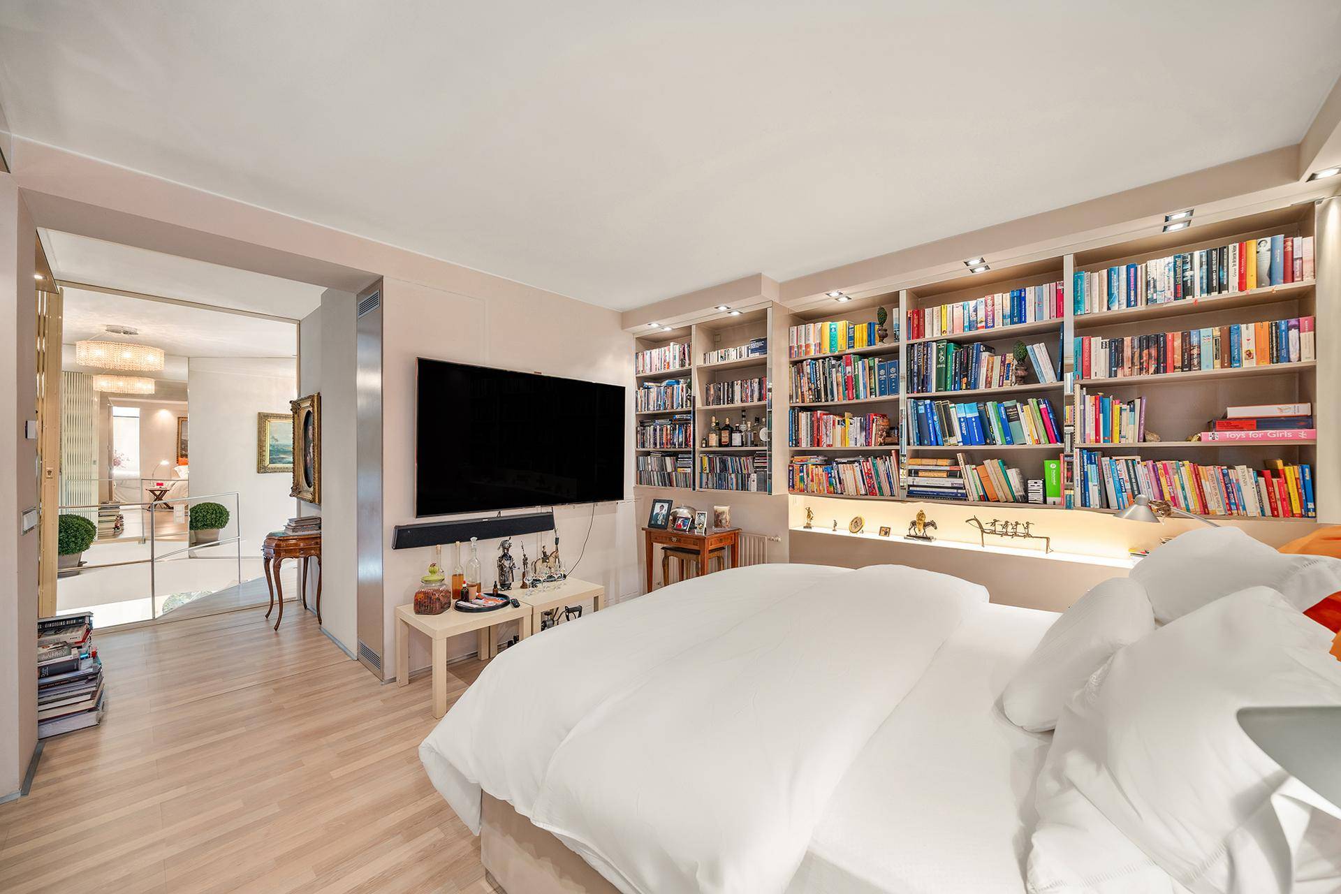 Gemütliches Schlafzimmer mit umfangreicher Bücherwand, Fernseher und hellem Holzfußboden.
