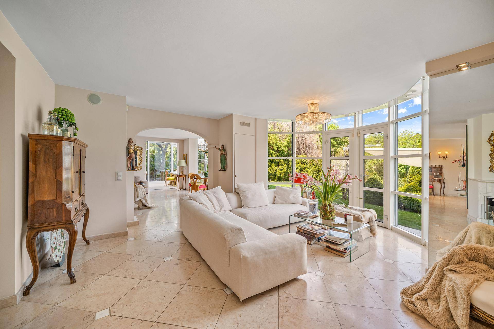 Helles Wohnzimmer mit großen Fenstern, die den Blick in den grünen Garten freigeben, und elegantem Fliesenboden.
