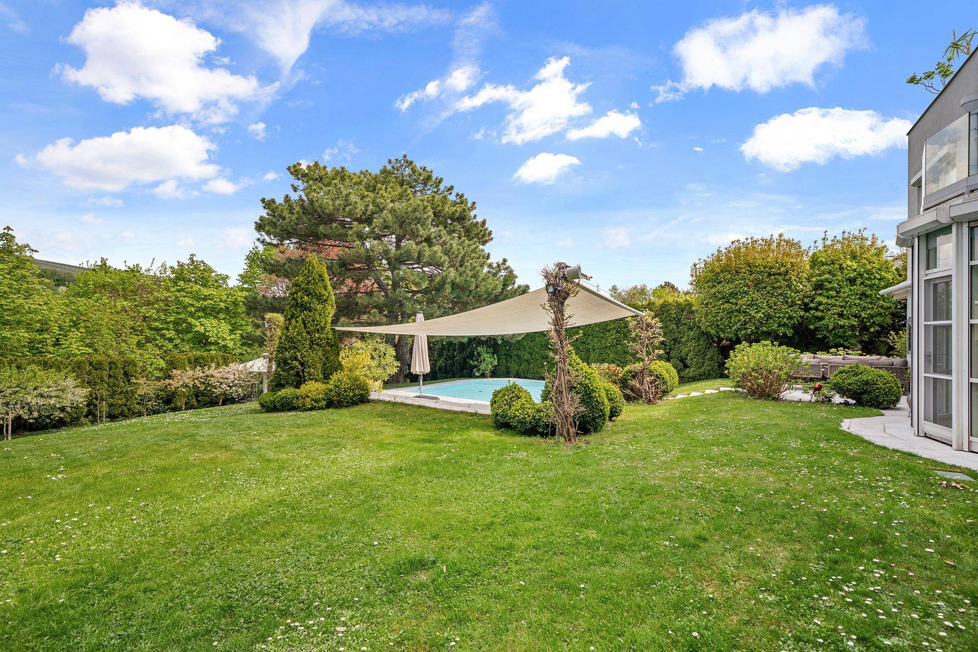 Weitläufiger Gartenbereich mit Pool und großem Sonnensegel, umgeben von üppigem Grün und Bäumen.