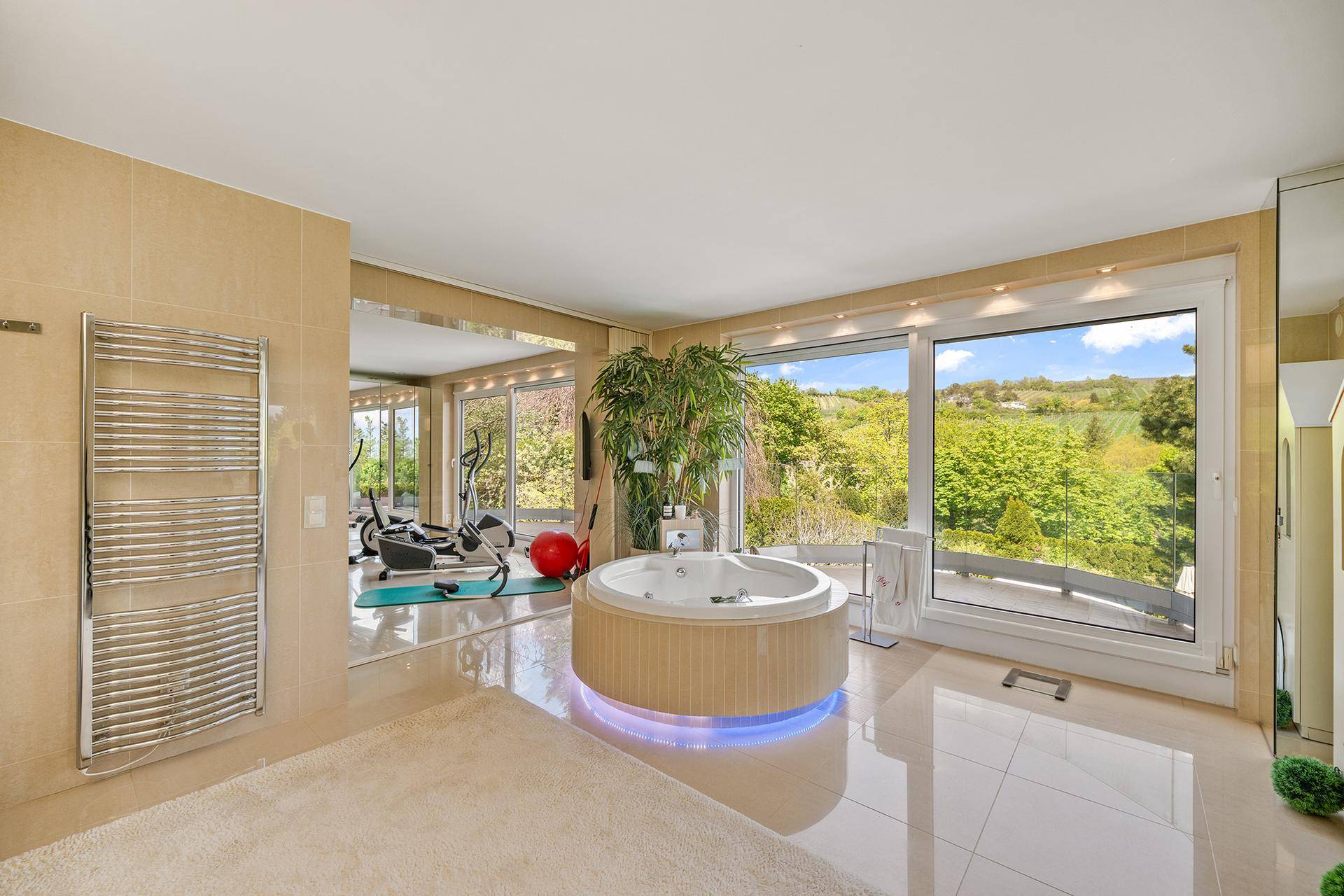 Luxuriöses Badezimmer mit Whirlpool, beheiztem Handtuchhalter und angrenzendem Fitnessbereich mit Aussicht.