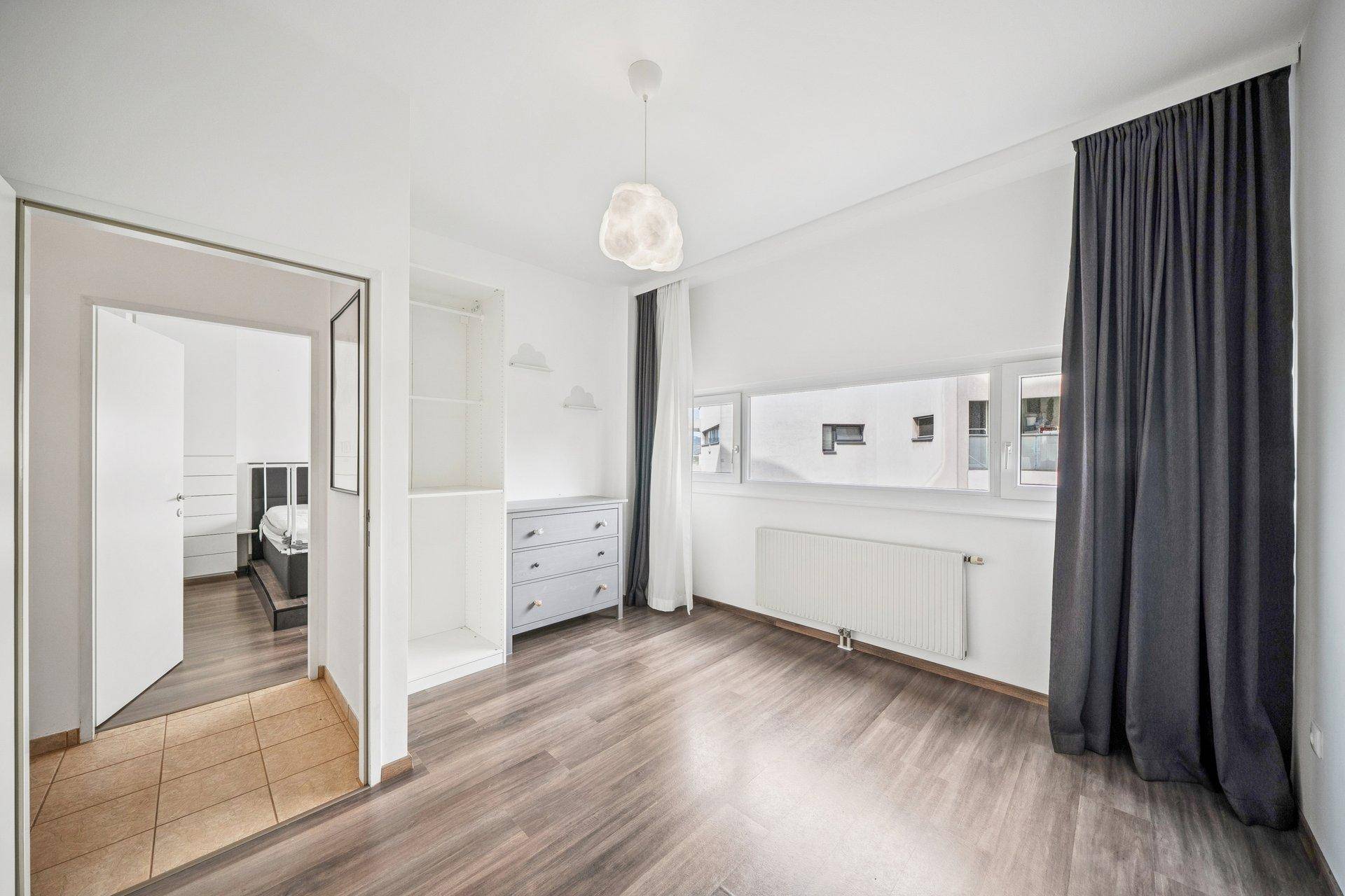 Helles Schlafzimmer mit Laminatboden, großen Fenstern und offenem Stauraum.