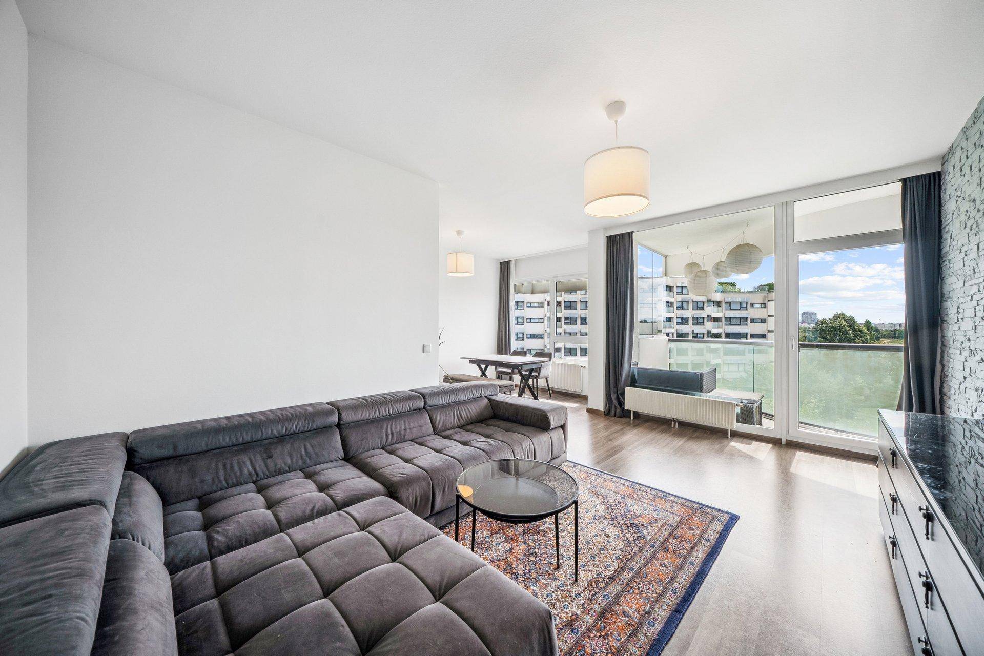 Geräumiges Wohnzimmer mit großem Ecksofa, Holzboden und Zugang zum Balkon mit Weitblick.