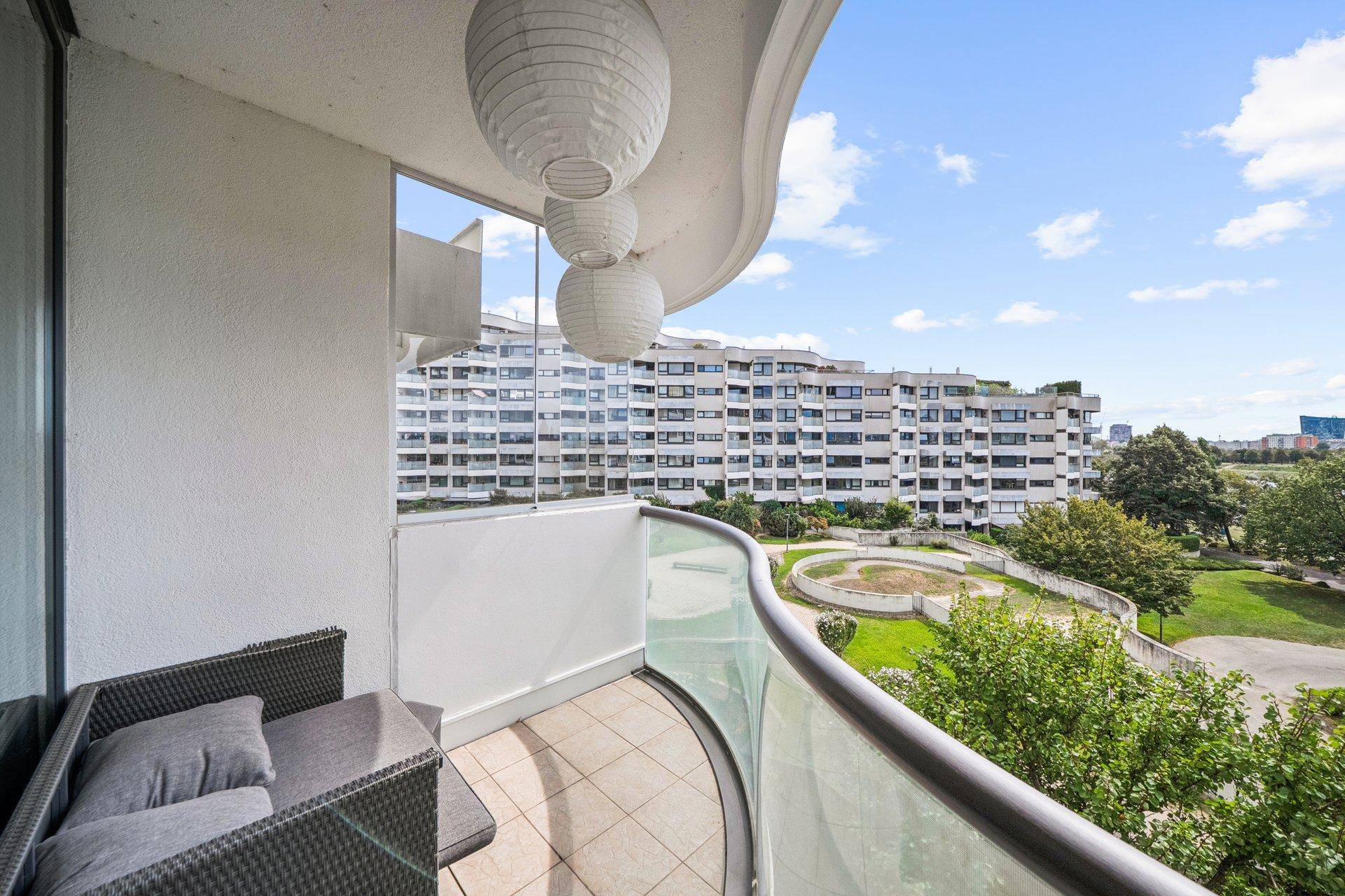 Gemütlicher Balkon mit Sitzgelegenheiten, Fliesenboden und Blick auf die umliegenden Gebäude und Grünflächen.